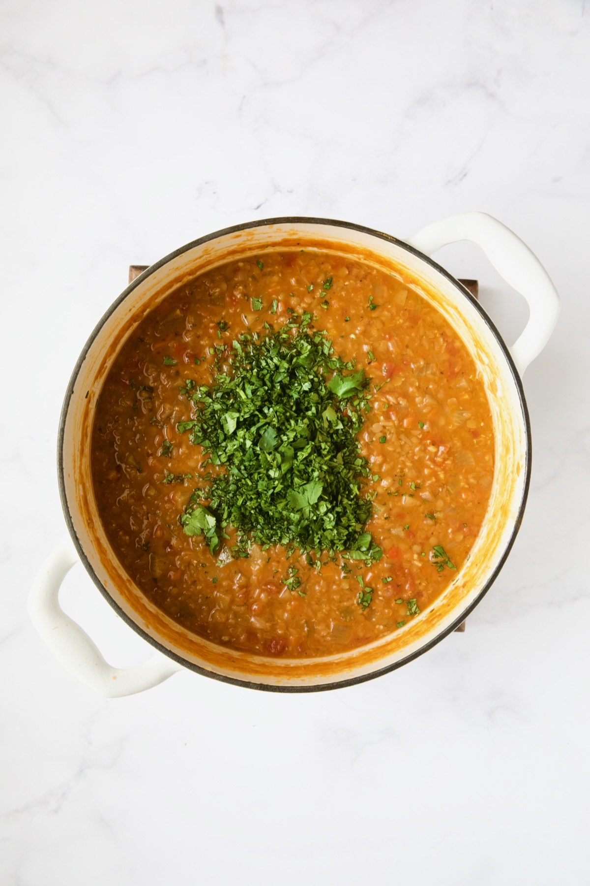 Ethiopian Red Lentil Vegetable Soup in white Dutch oven with cilantro sprinkled over the top.