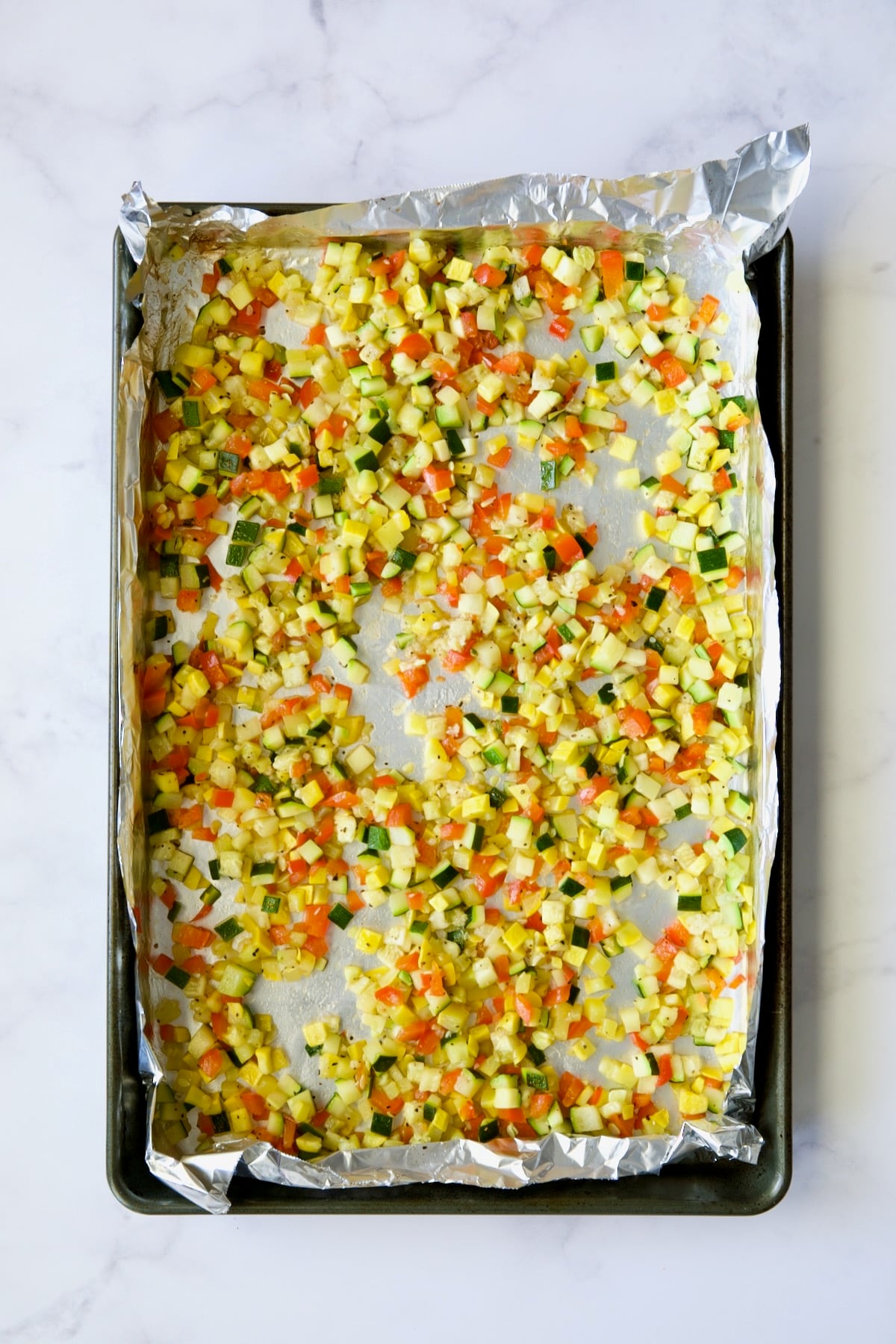 Diced roasted zucchini, yellow squash and red bell pepper on aluminum foil-lined baking sheet.