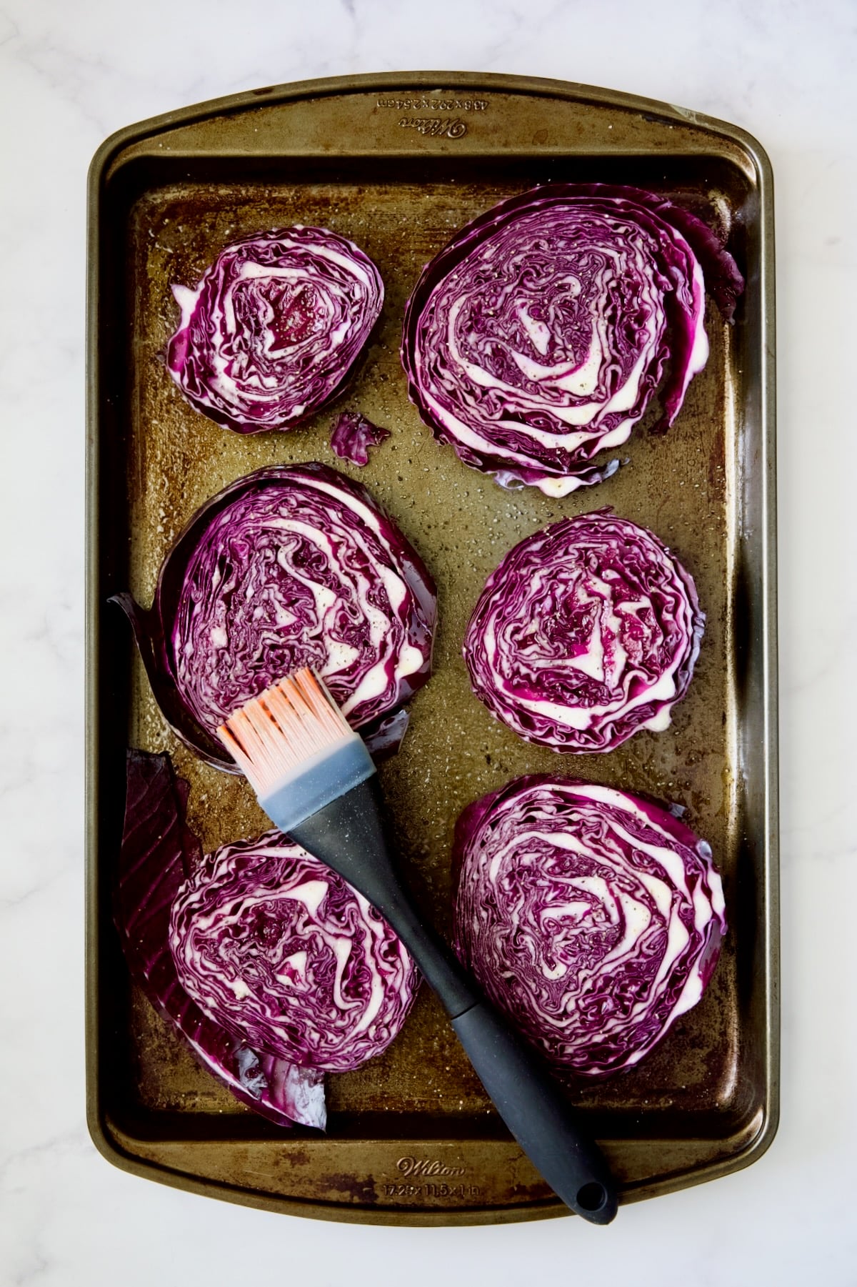 Red cabbage wedges on baking sheet being brushed with olive oi.