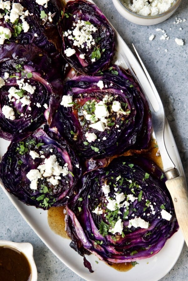 Roasted Red Cabbage Steaks with Balsamic Vinaigrette and Goat Cheese on white platter with serving fork.