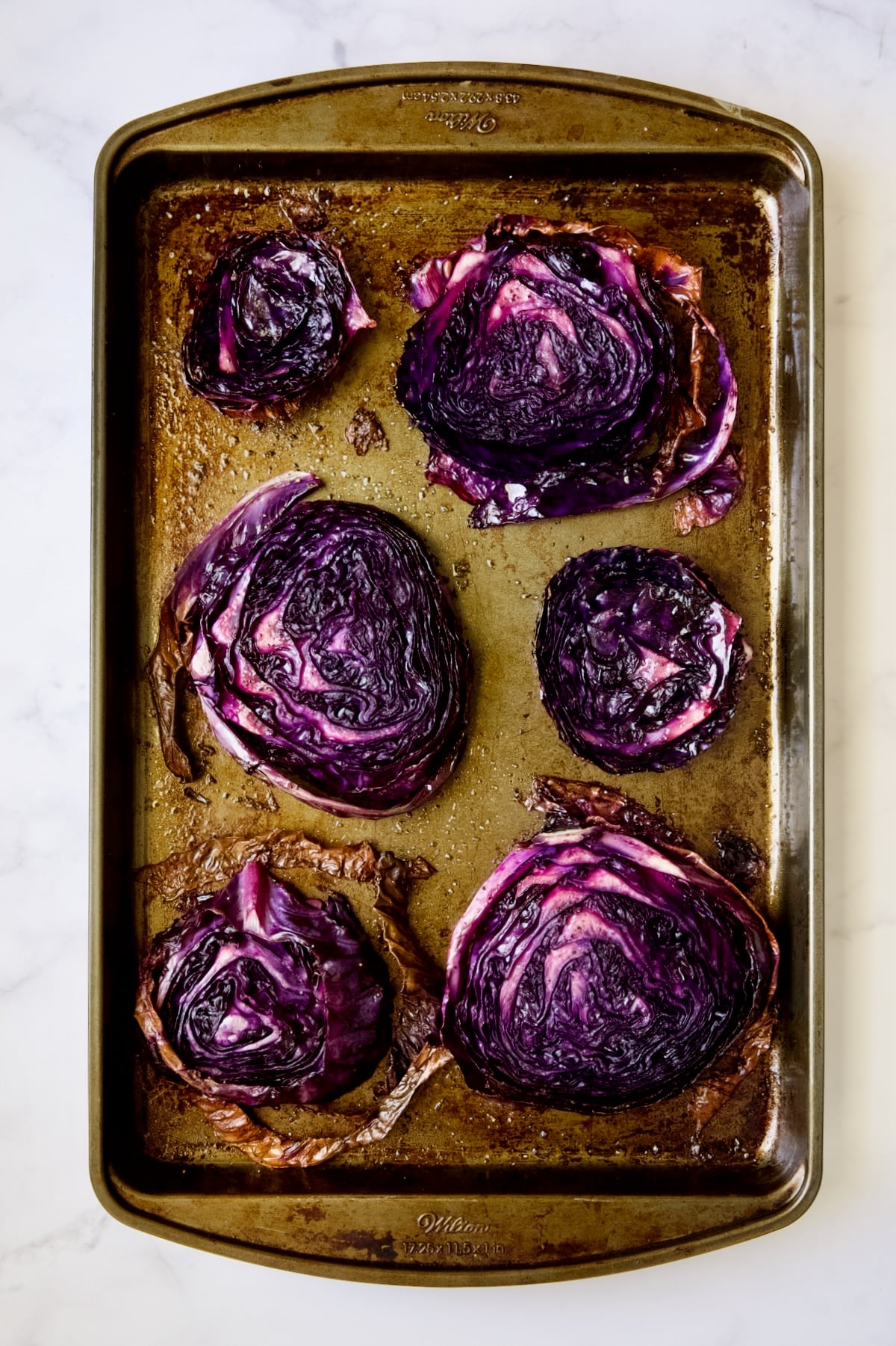 Six roasted red cabbage steaks on baking sheet.