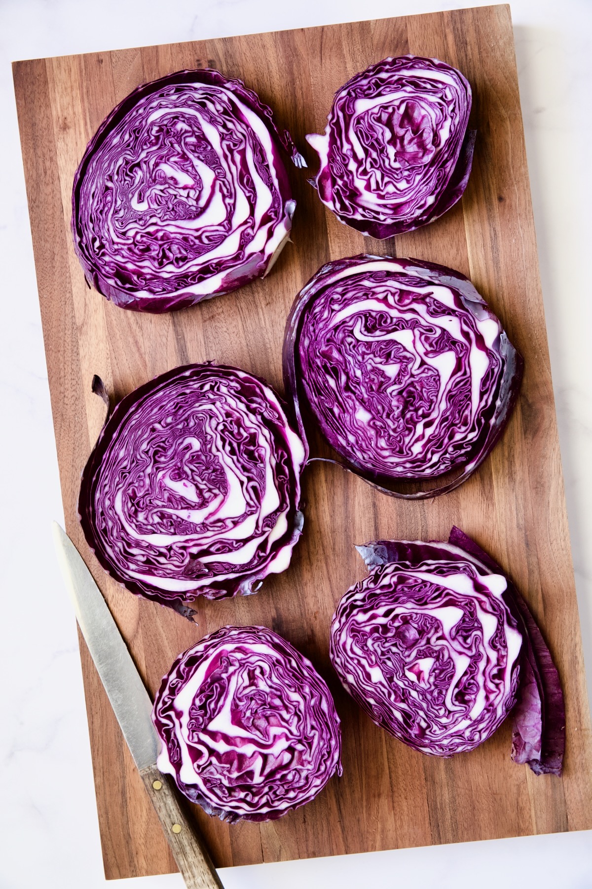 Six red cabbage slices on wood cutting board.