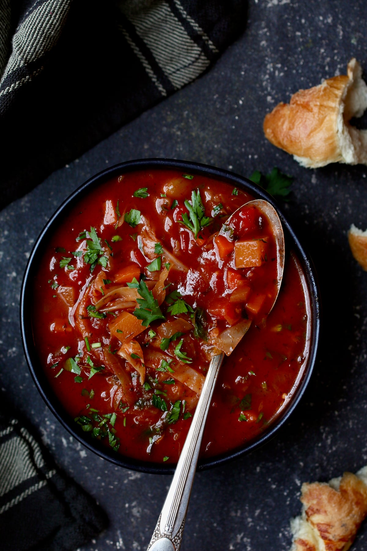 Rustic Cabbage and Root Vegetable Soup in black bowl garnished with parsley.