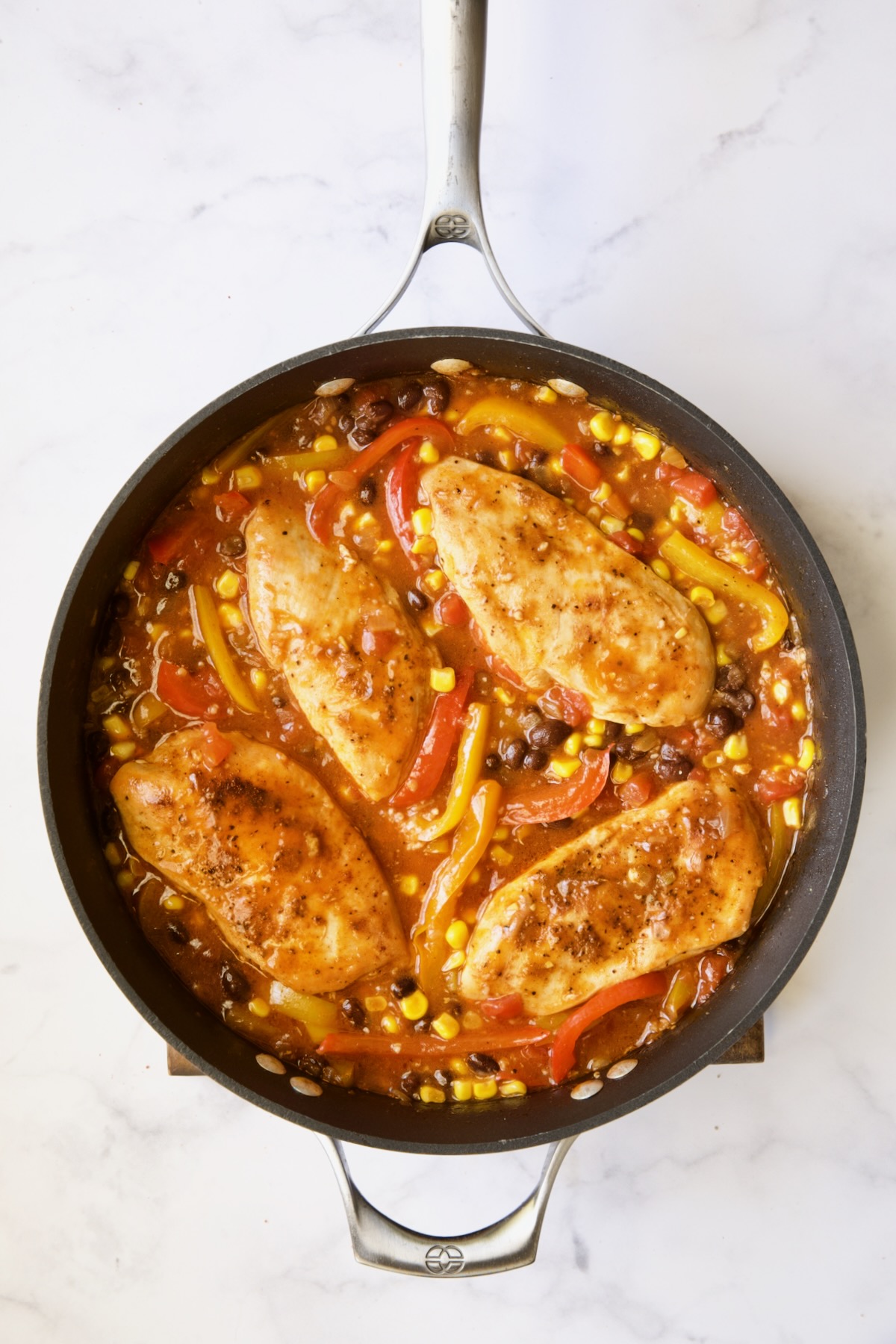 Four cooked chicken breasts with other ingredients in skillet.