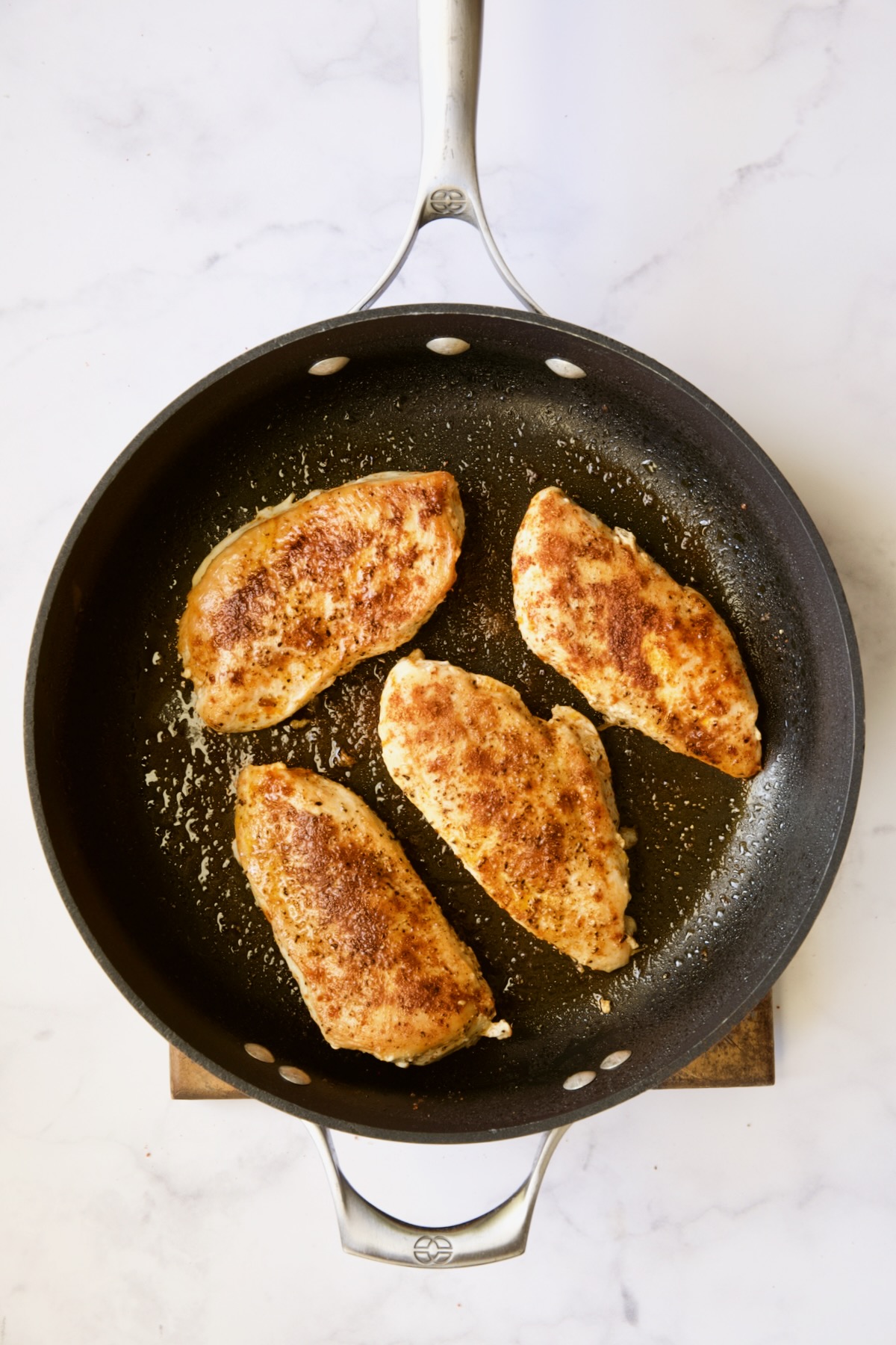 Four cooked chicken breasts in skillet.
