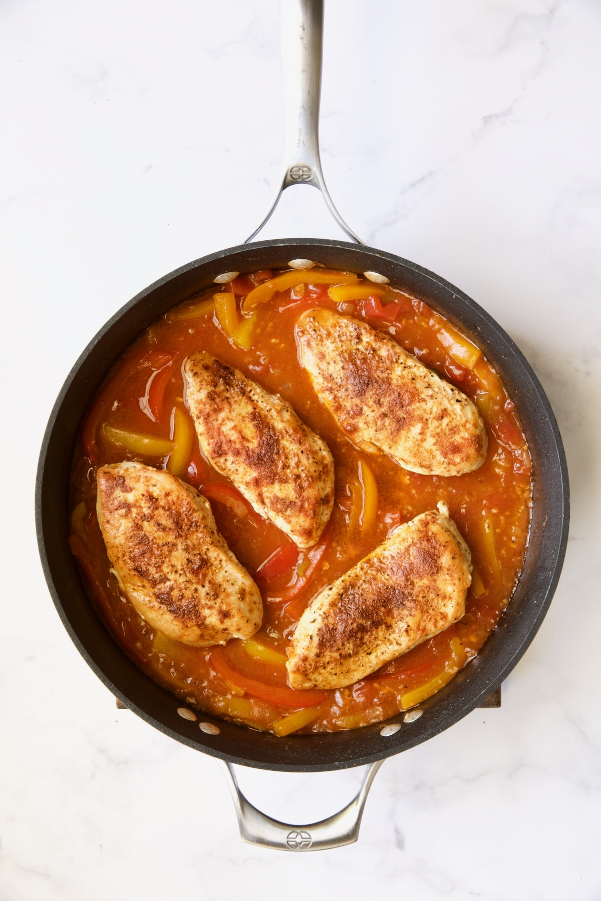 Four cooked chicken breasts in sauce in skillet.