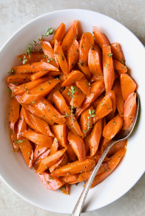 Bourbon-Glazed Carrots with Honey in white serving bowl with fresh thyme.