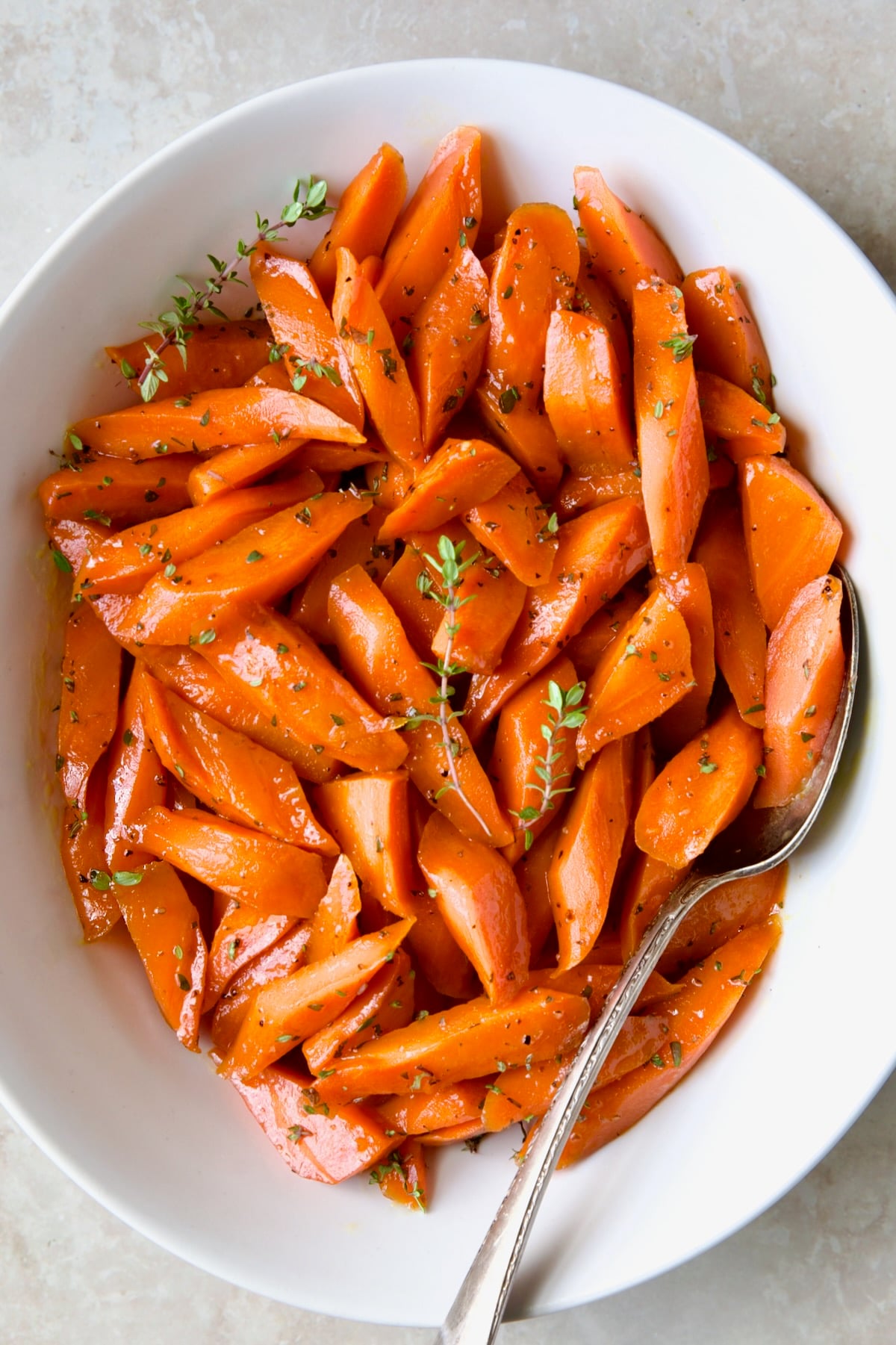 Bourbon-Glazed Carrots with Honey in white serving bowl with fresh thyme.