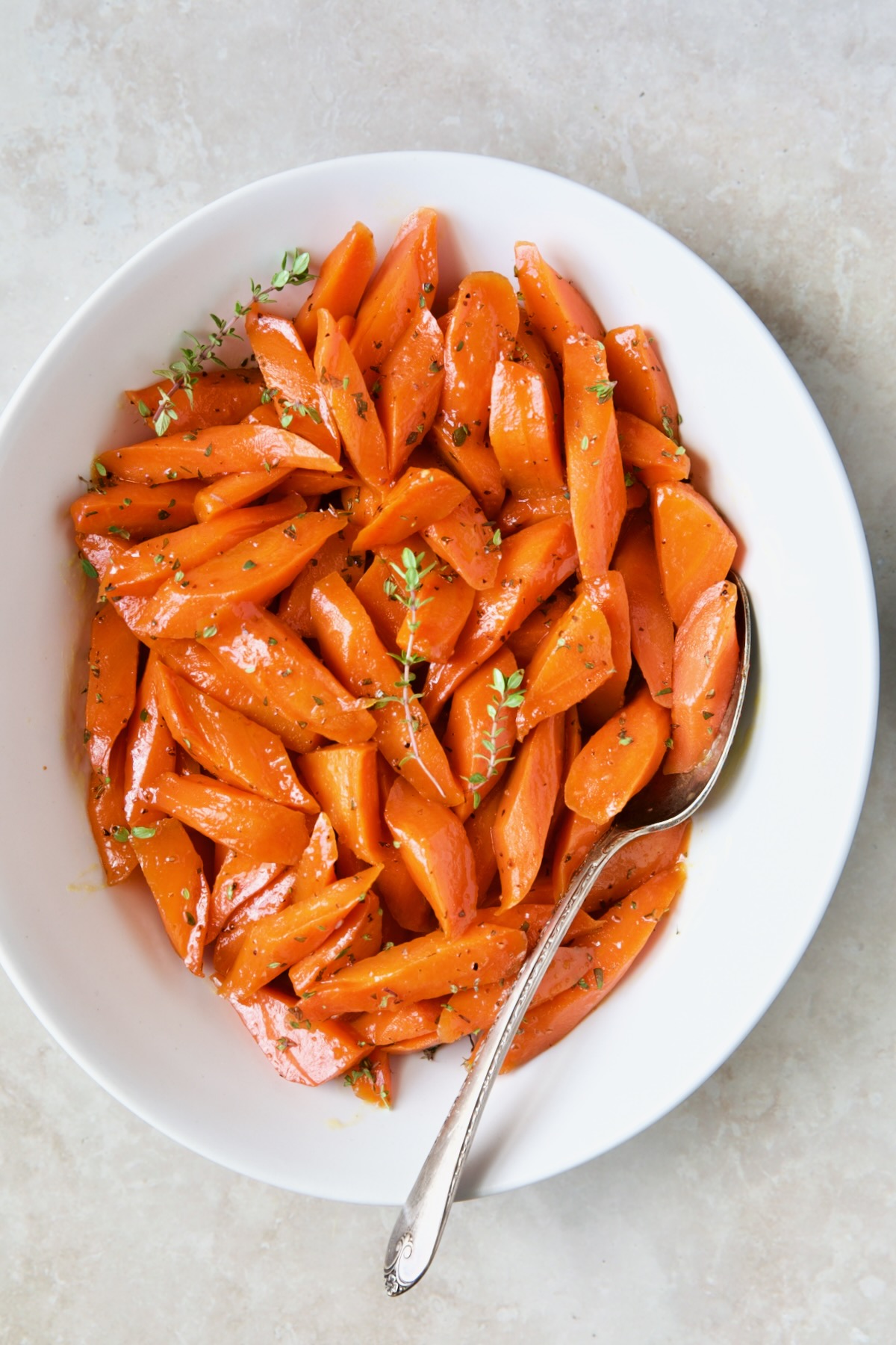 Bourbon-Glazed Carrots with Honey in white serving bowl garnished with fresh thyme.