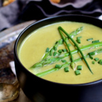Cream of Asparagus and Leek Soup with Curry in black bowl garnished with chives.