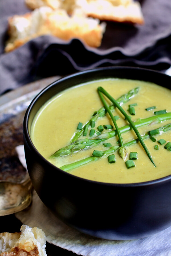 Cream of Asparagus and Leek Soup with Curry in black bowl garnished with chives.