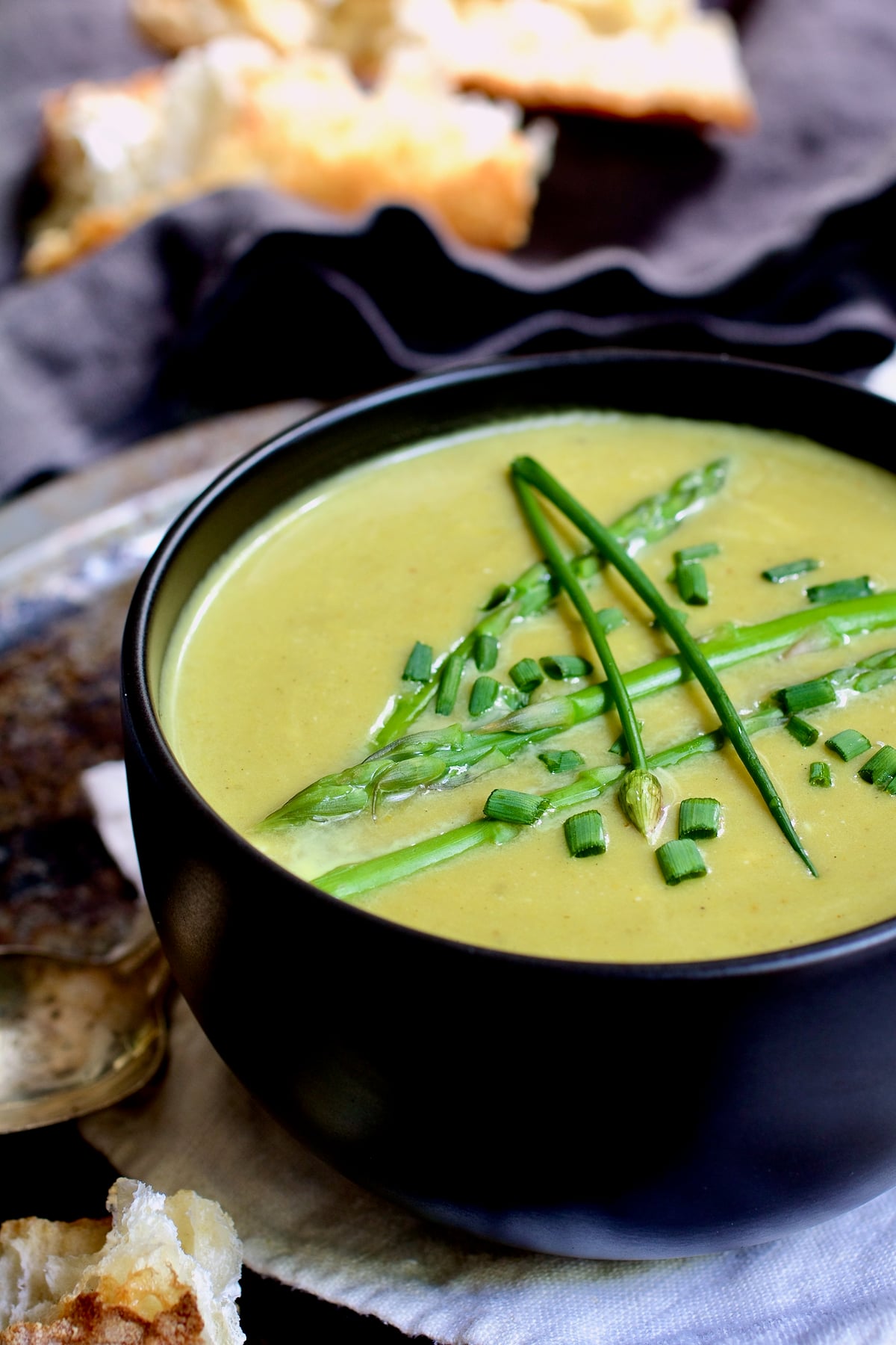 Cream of Asparagus and Leek Soup with Curry in black bowl garnished with chives.