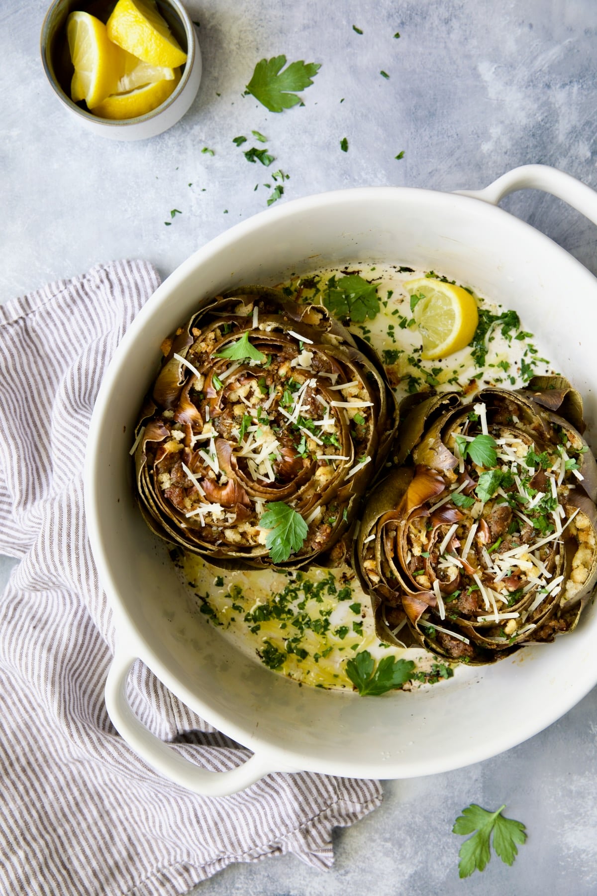 Two Italian-Stuffed Artichokes in white baking dish garnished with fresh parsley.
