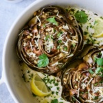 Baked Italian-Stuffed Artichokes in white baking dish garnished with lemon wedges.
