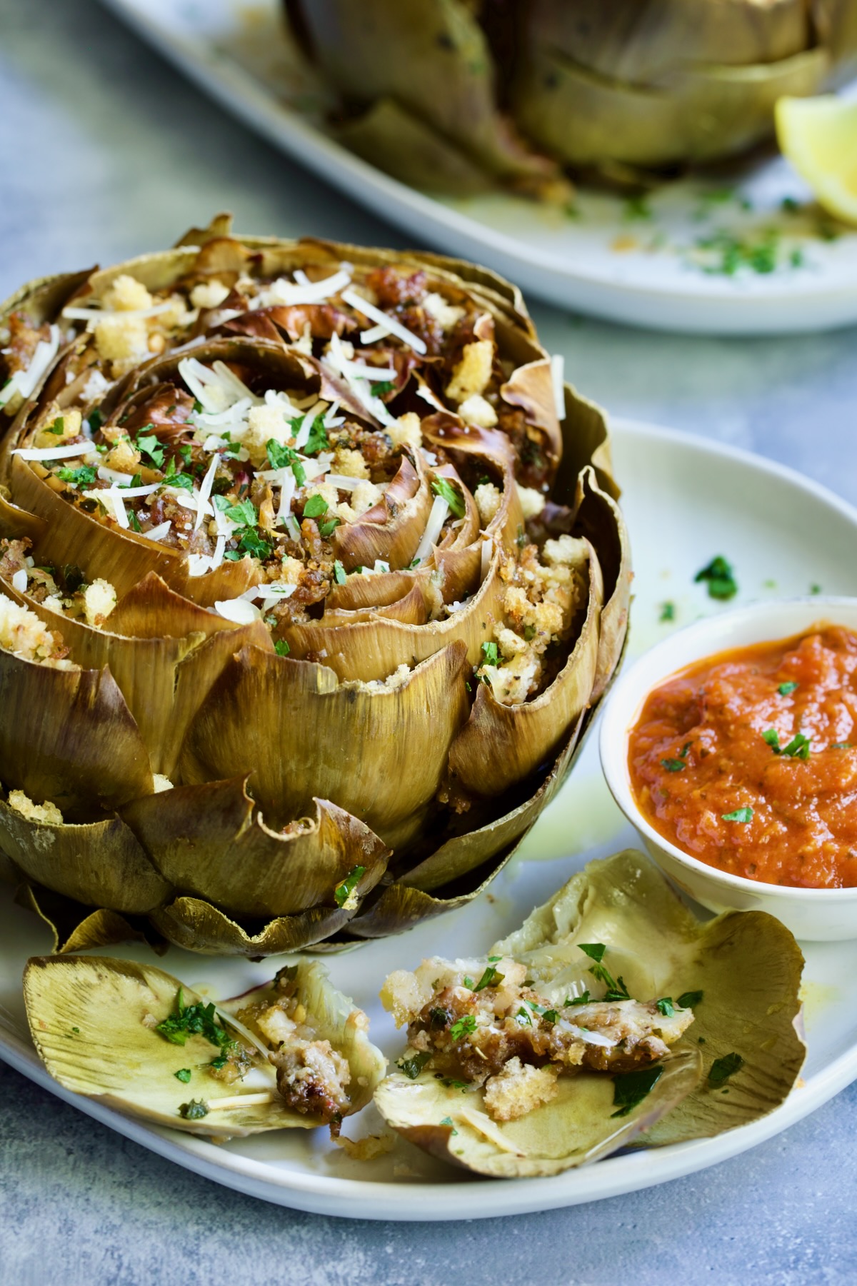 Stuffed artichoke on white plate with marinara sauce.