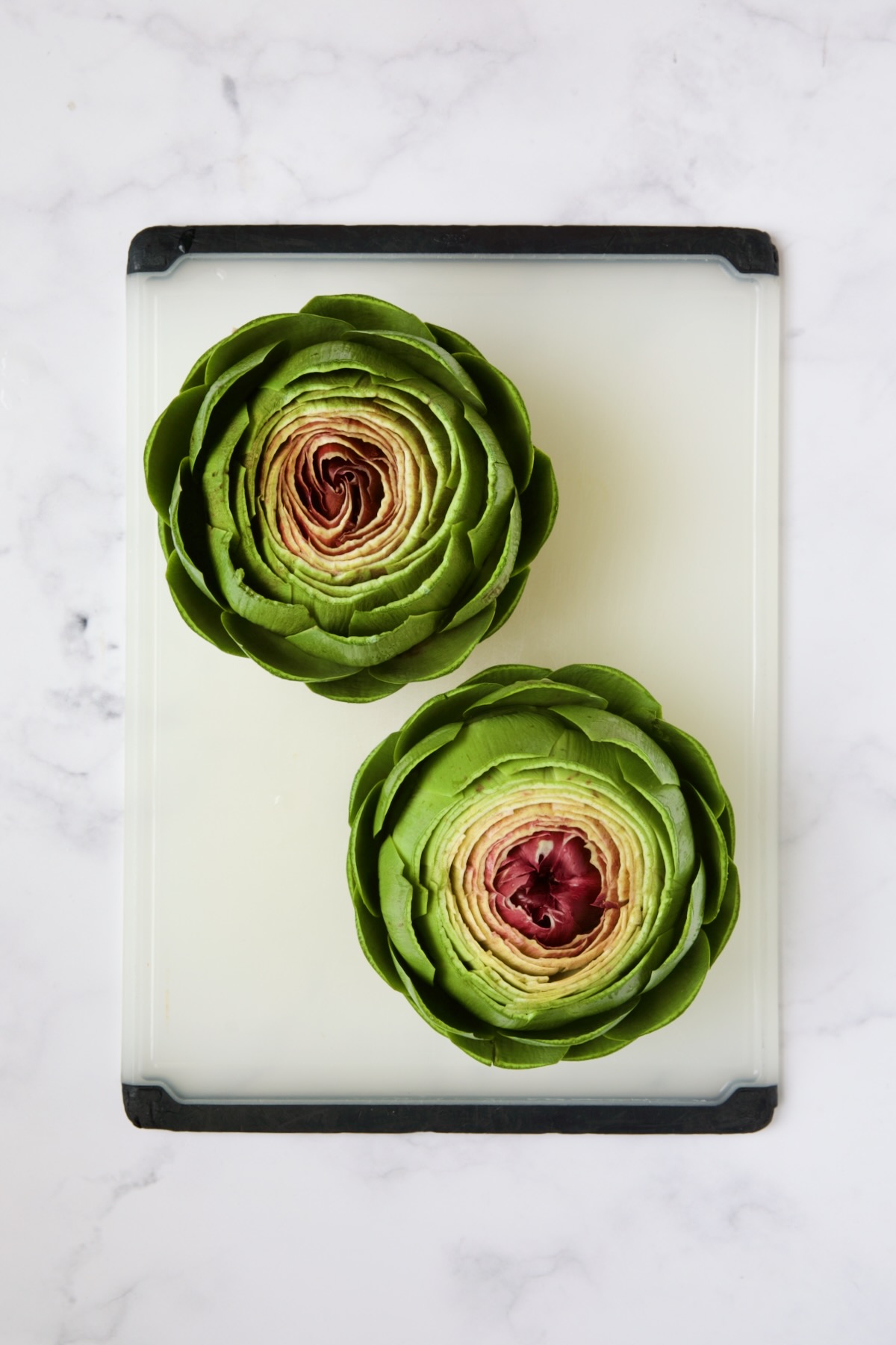 Two trimmed artichokes on white cutting board.