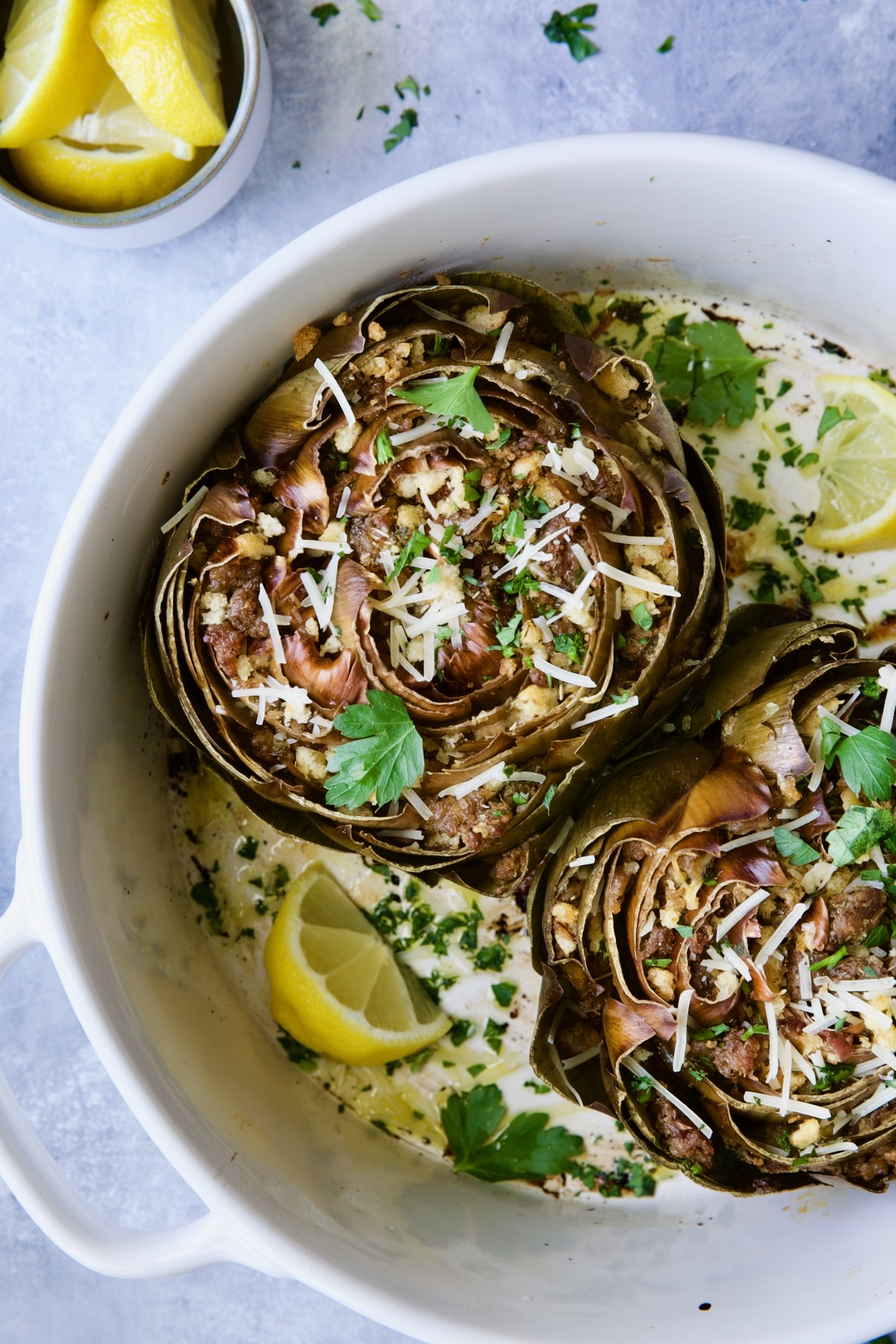 Baked Italian-Stuffed Artichokes in white baking dish garnished with lemon wedges.