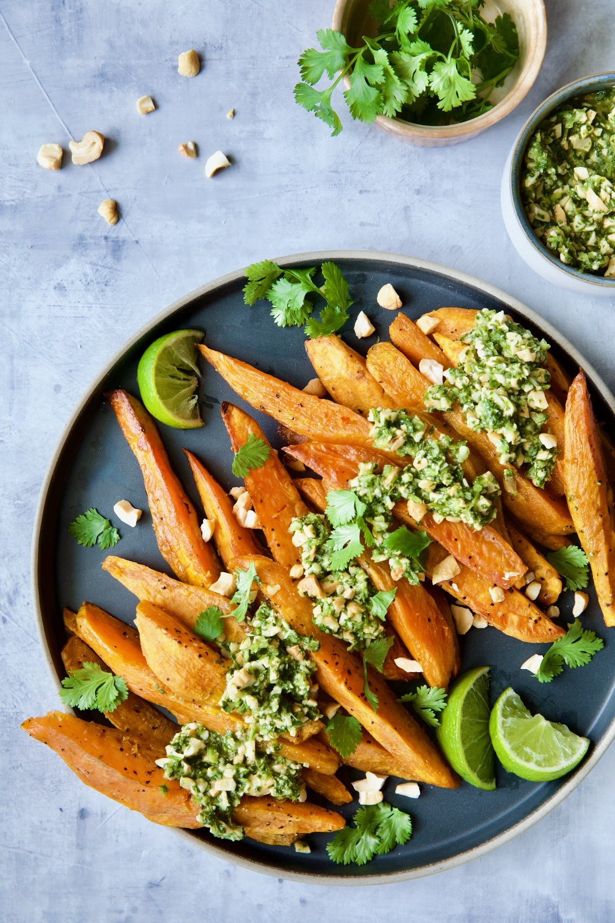 Roasted Sweet Potato Wedges with Cilantro - Cashew Sauce on round plate garnished with lime wedges and cilantro.