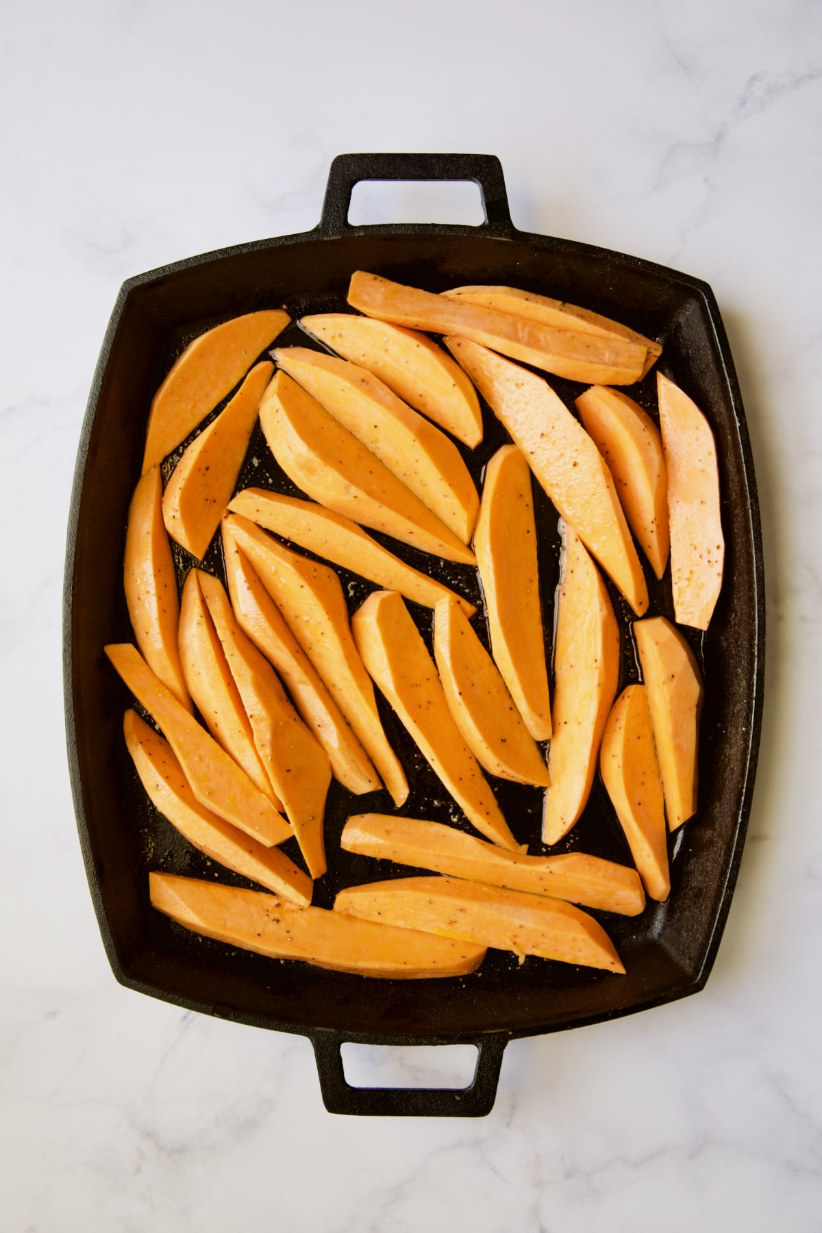 Sweet potatoes on cast iron baking pan before being roasted.