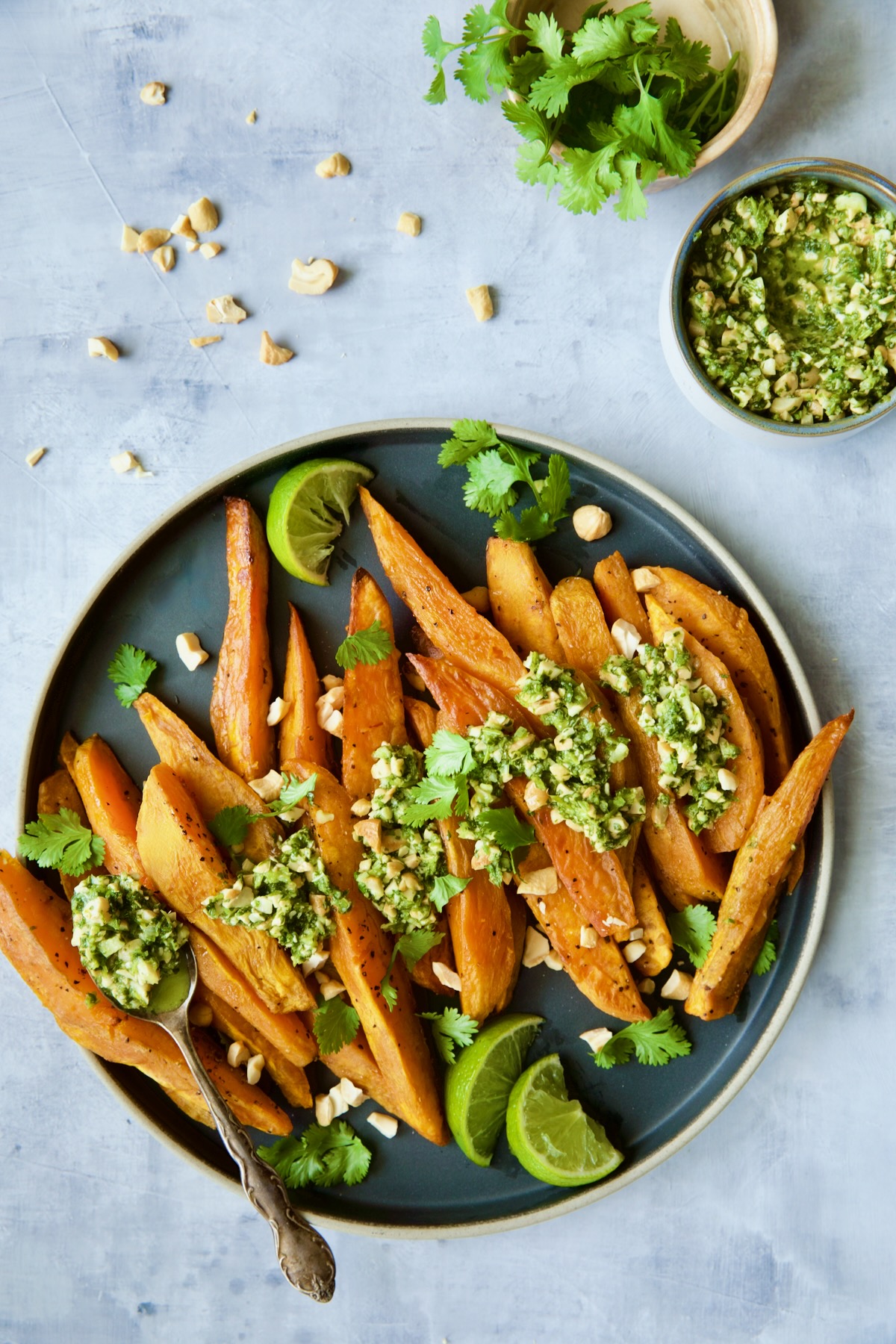 Roasted Sweet Potato Wedges with Cilantro - Cashew Sauce on round plate with spoon dishing sauce over the potatoes.