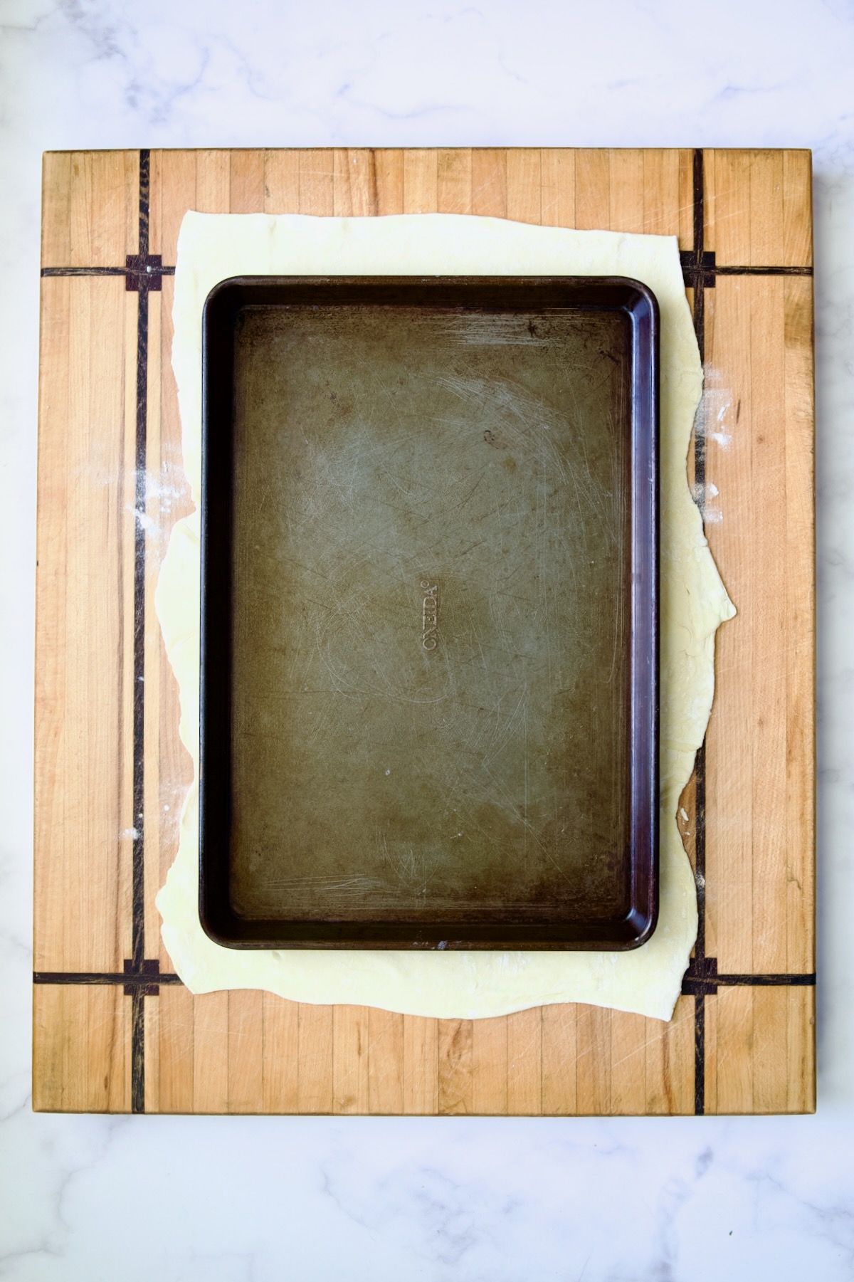 Sheet pan set over puff pastry crust on wood cutting board.