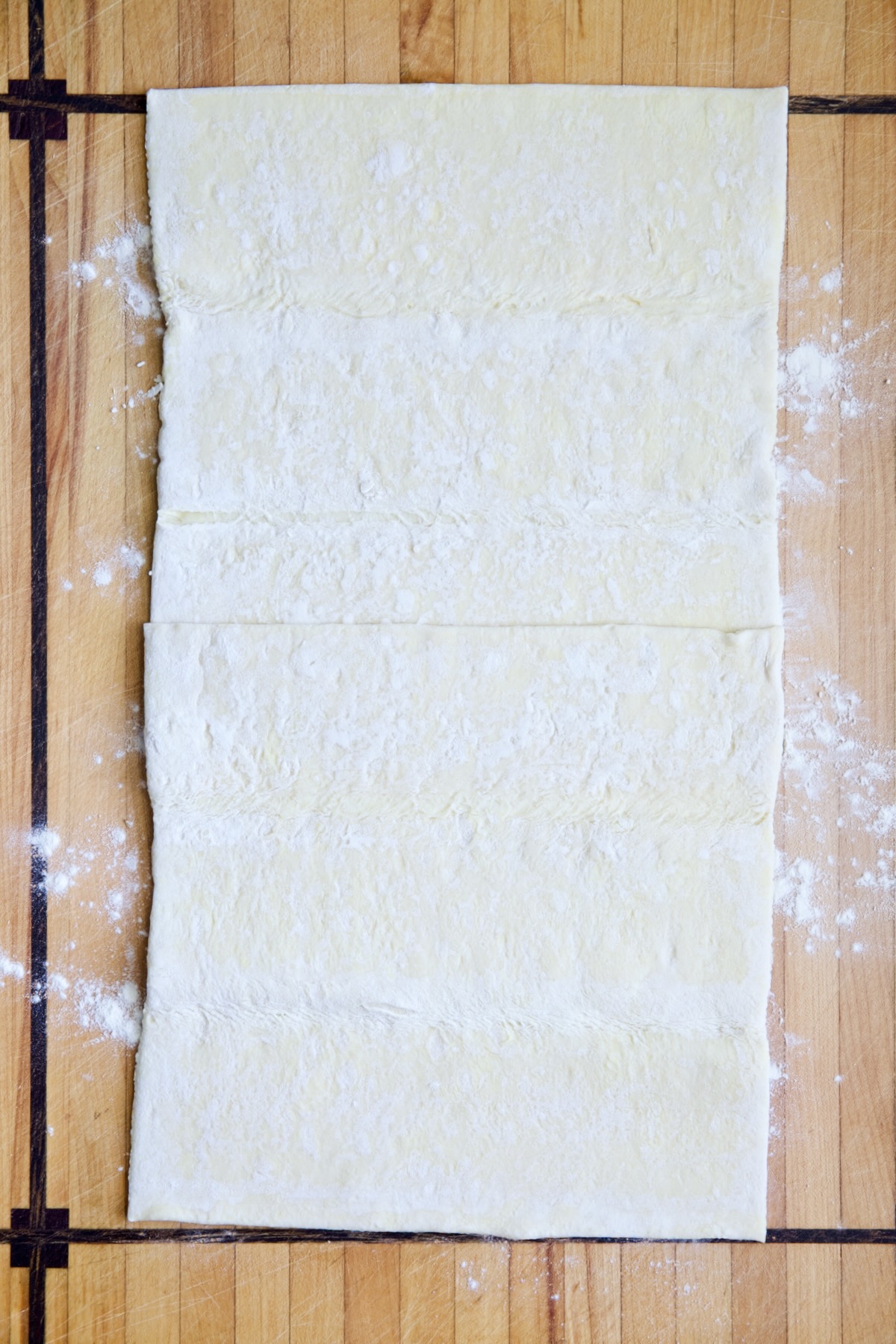 Puff pastry crust on wood cutting board before being rolled out.