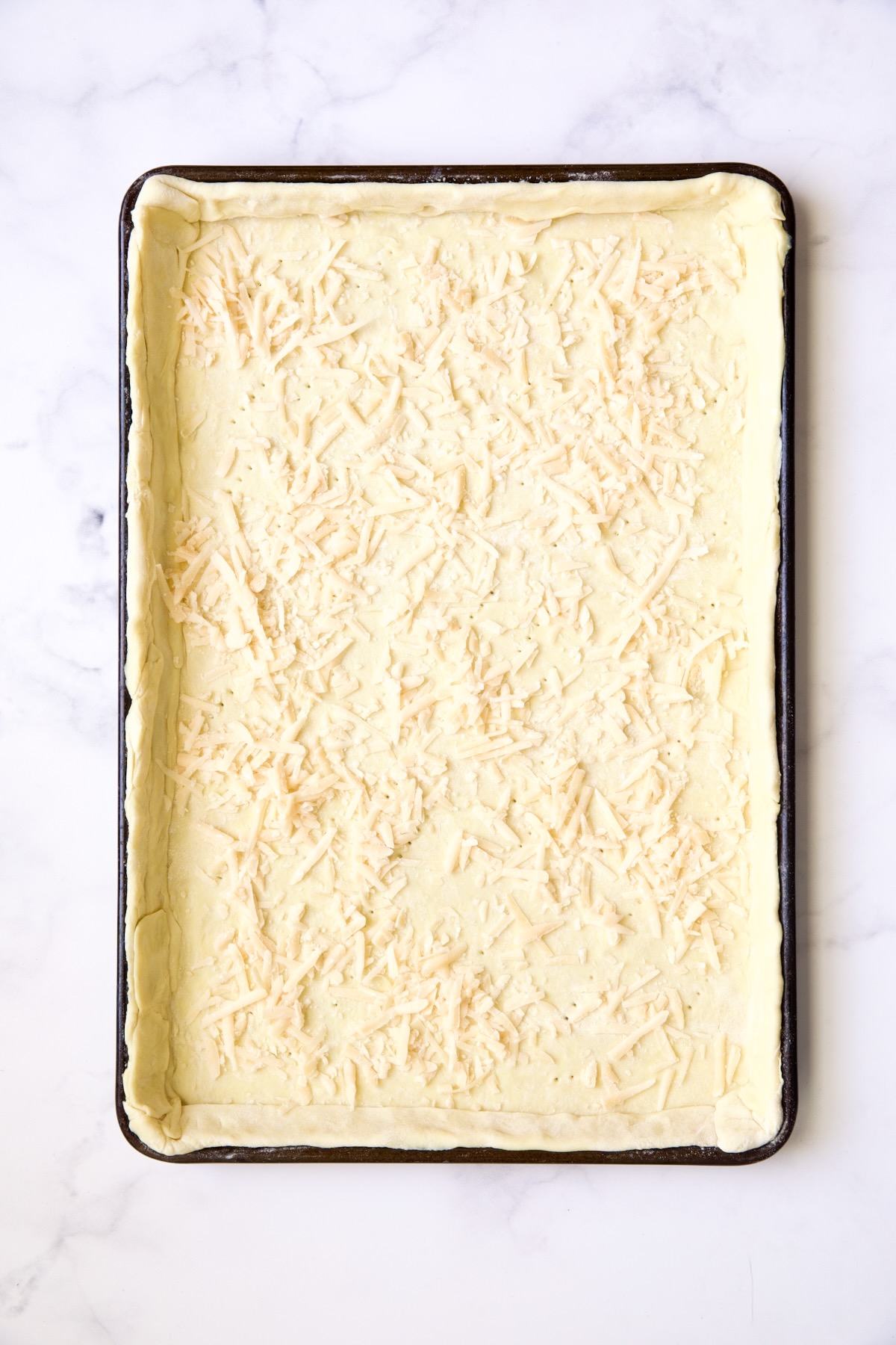 Puff pastry crust with layer of cheese sprinkled over it.