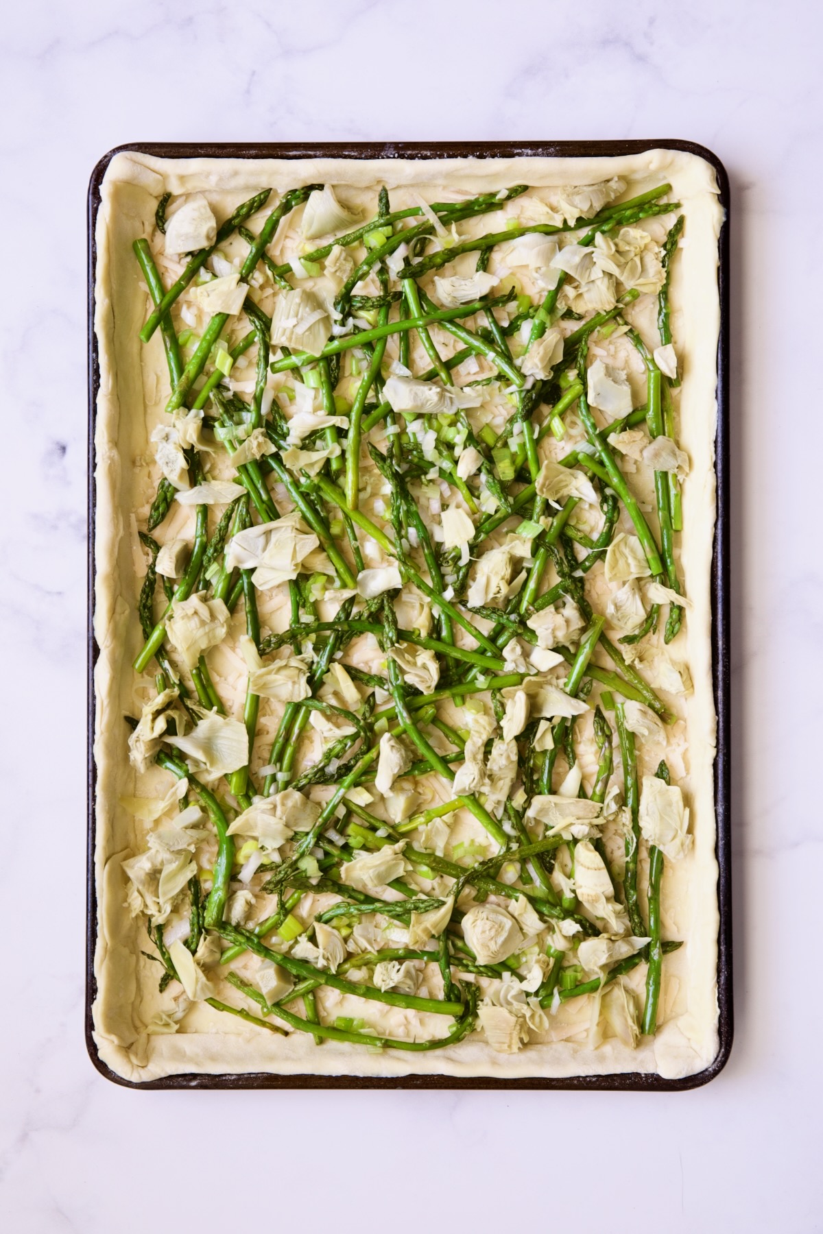 Tart before being baked with asparagus, artichokes and scallions.