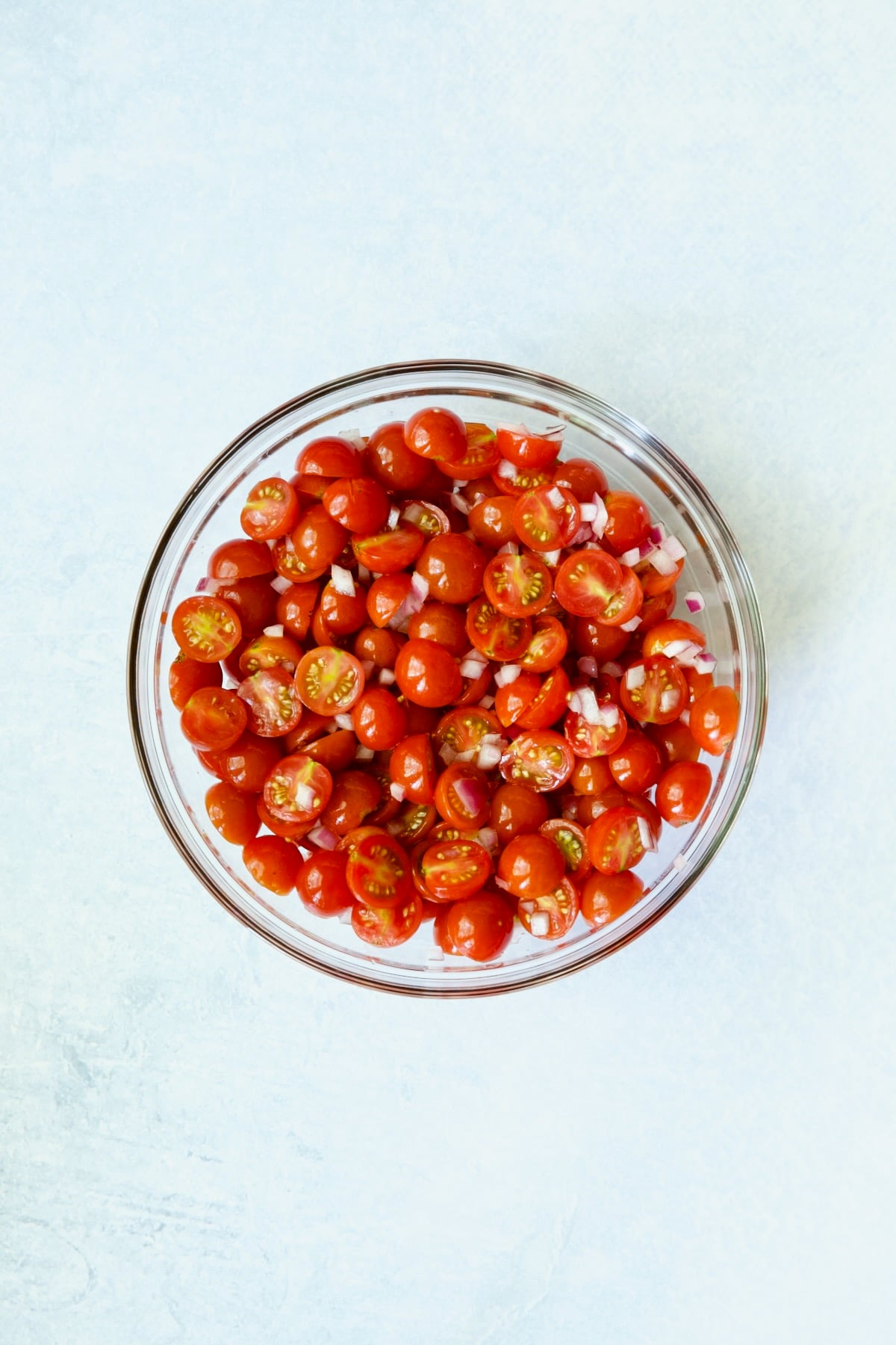 Cherry tomatoes and red onion in glass bowl.