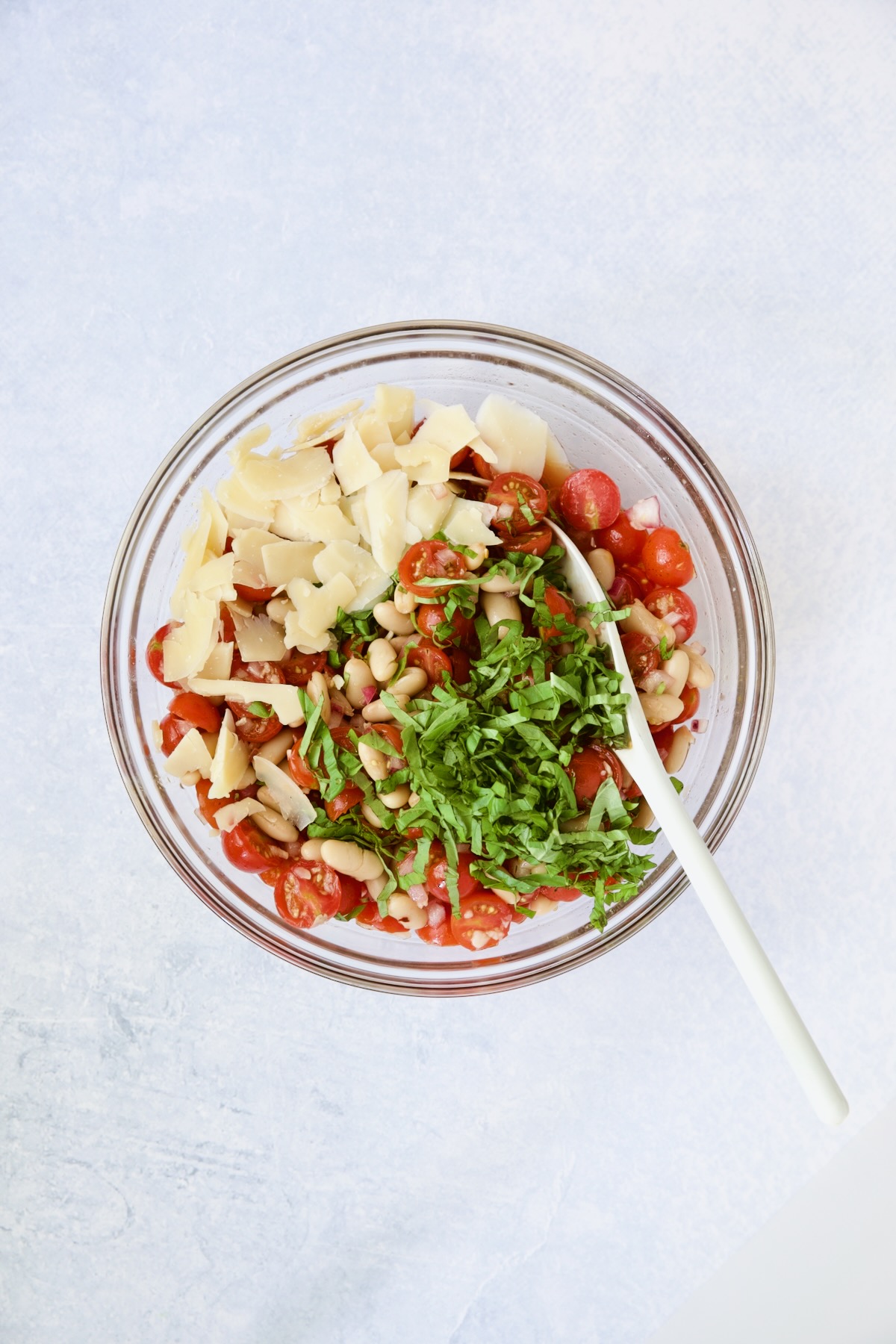 Salad in glass bowl being stirred with white spoon.