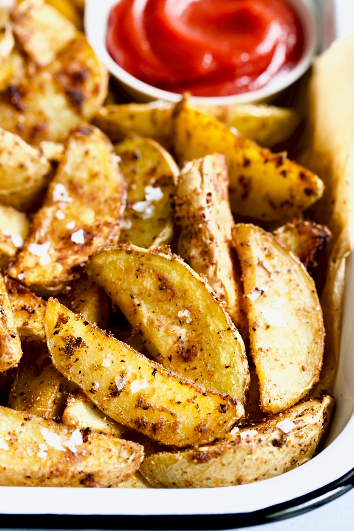 Perfect Roasted Potato Wedges on parchment paper in white enamel tray with ketchup.