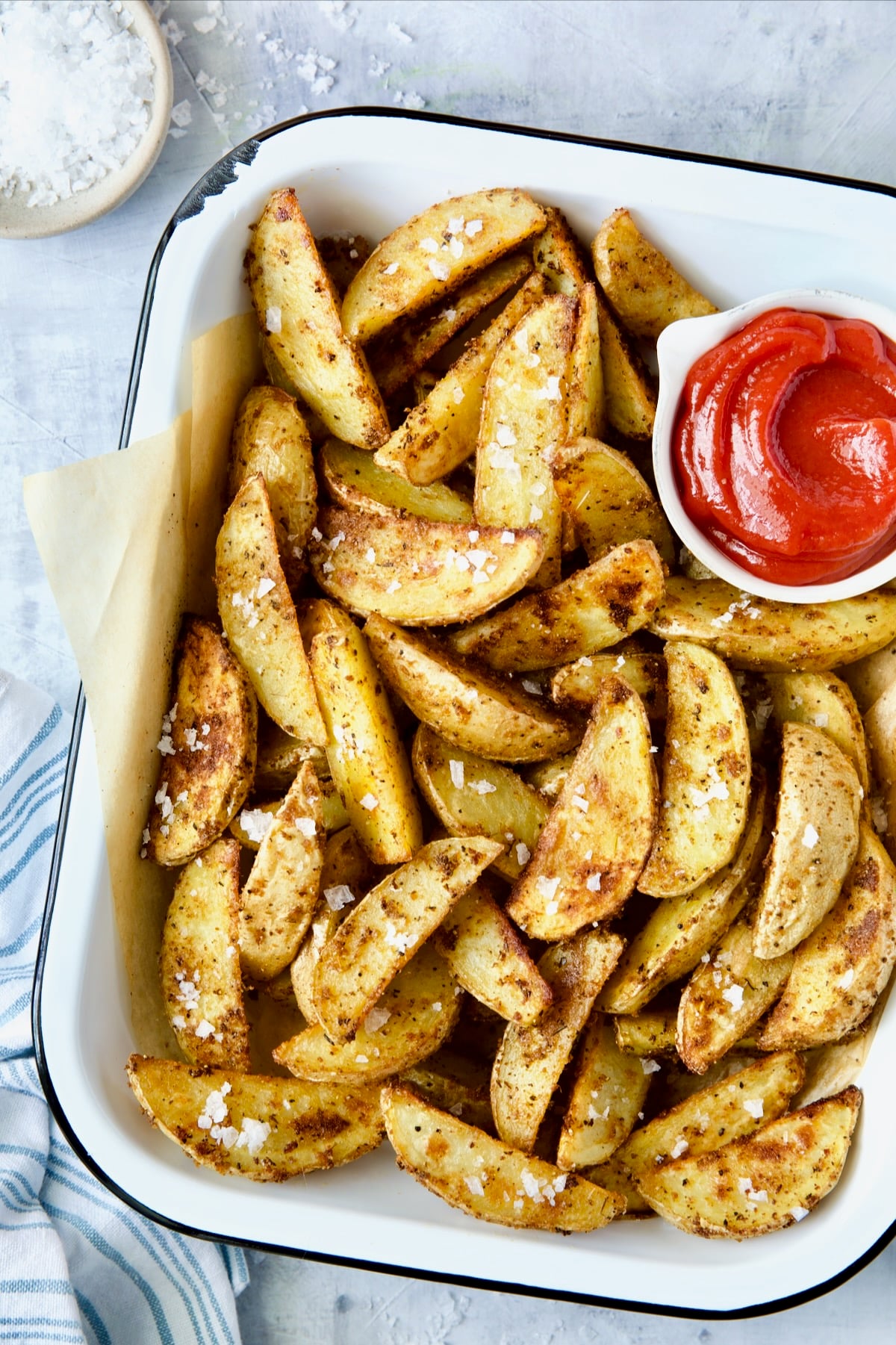 Perfect Roasted Potato Wedges in white enamel tray with ketchup and coarse sea salt.