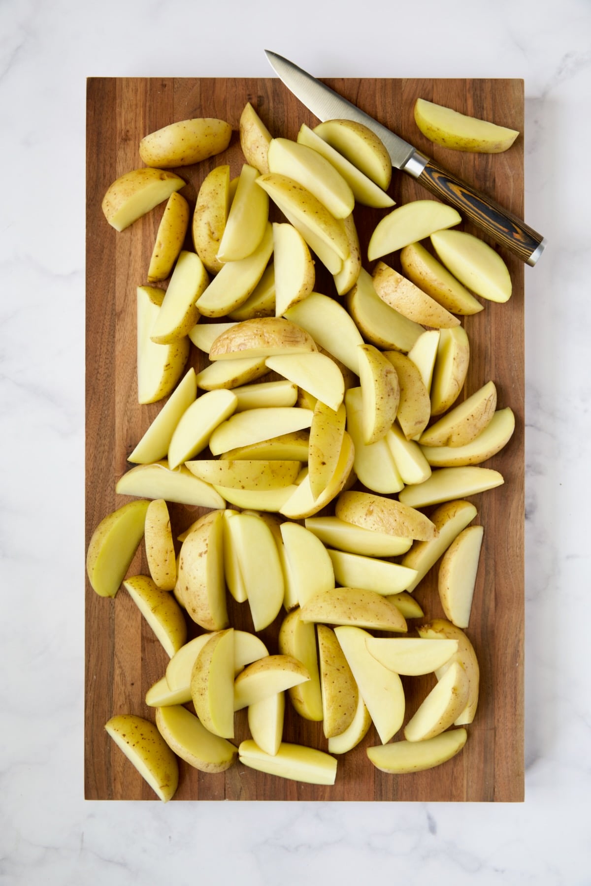 Yukon Gold potato wedges on wood cutting board with knife.