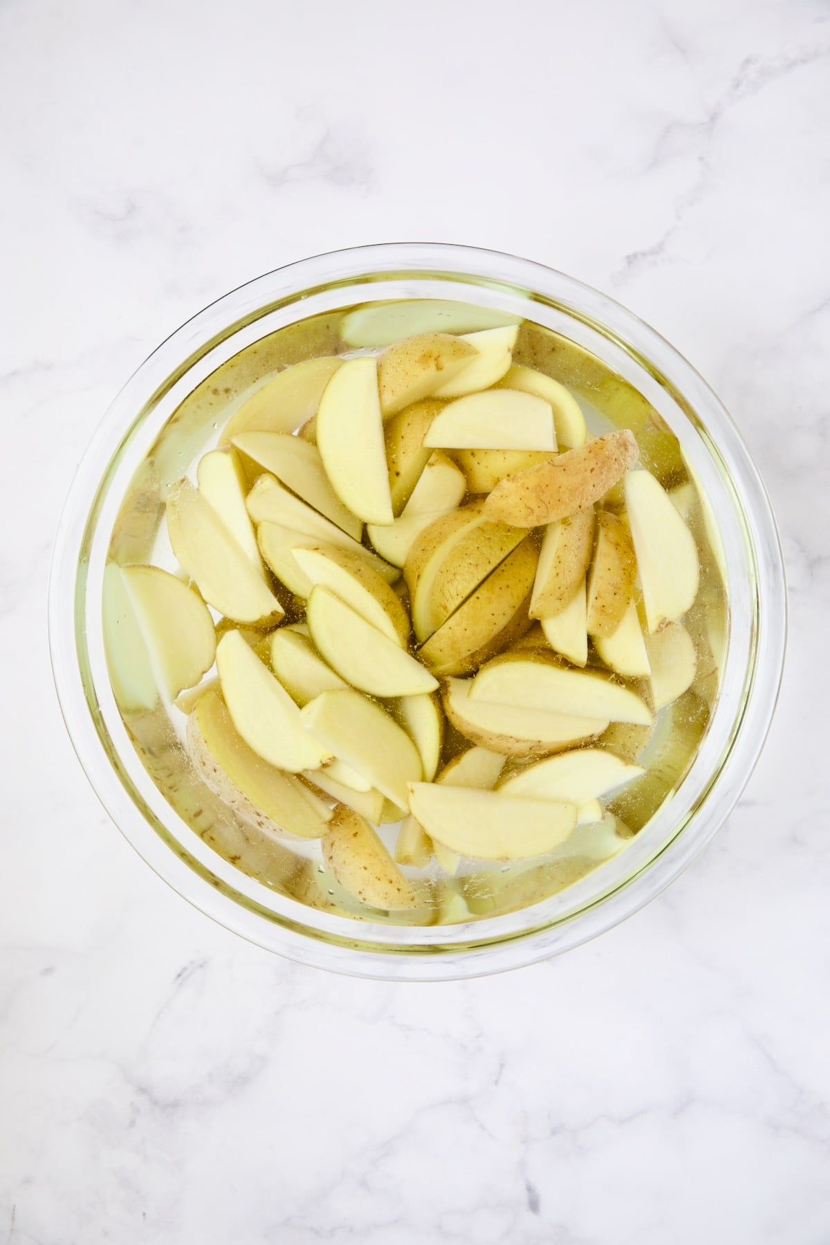 Yukon Gold potato wedges in water in glass bowl.