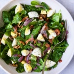 Radish Greens Salad with Hot Bacon Dressing in white serving bowl with serving fork.