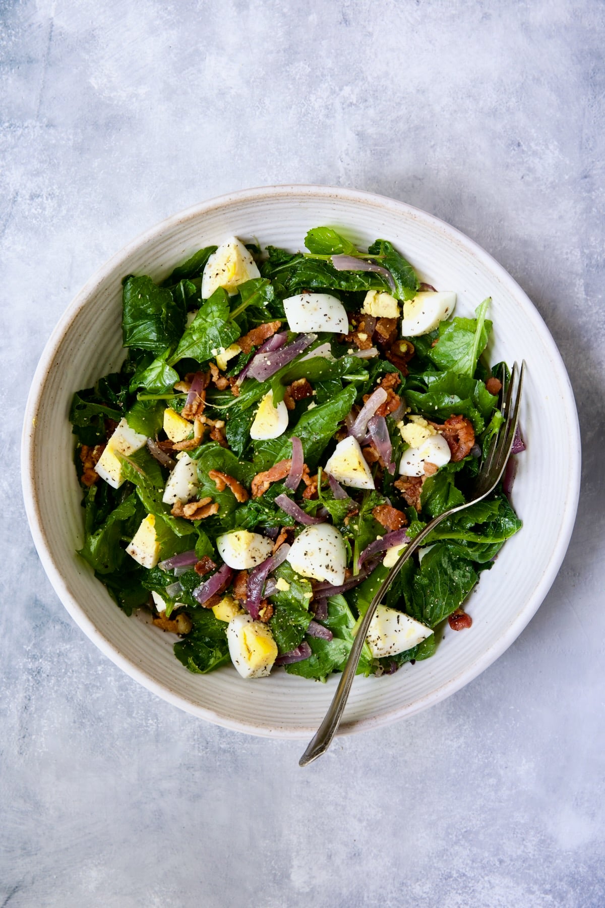 Radish Greens Salad with Hot Bacon Dressing in white serving bowl with fork.