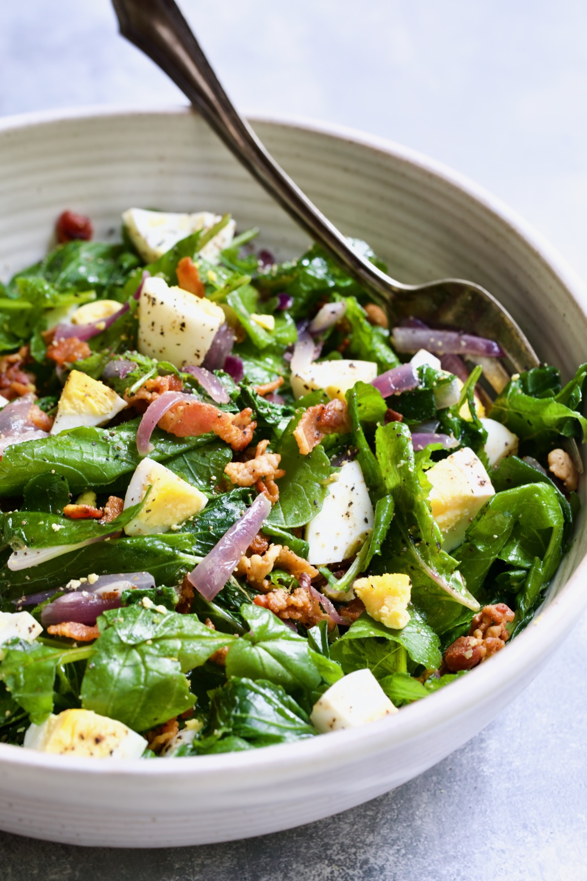 Radish Greens Salad with Hot Bacon Dressing in white serving bowl with serving fork.
