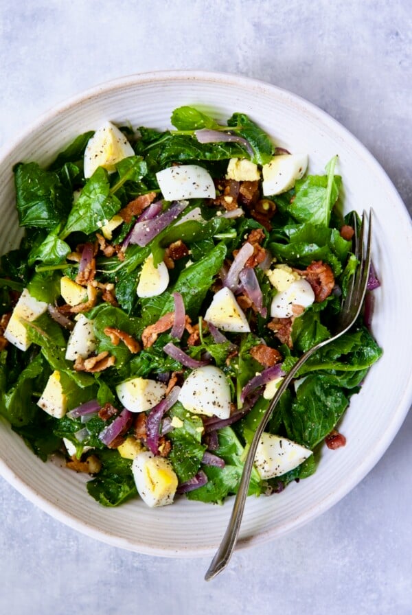 Radish Greens Salad with Hot Bacon Dressing in white serving bowl with serving fork.