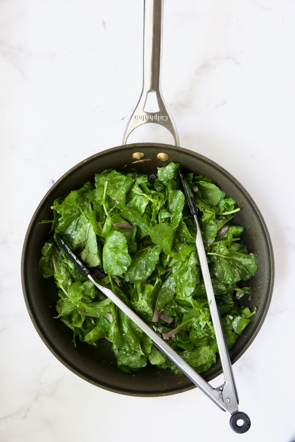 Slightly wilted radish greens in skillet with tongs.