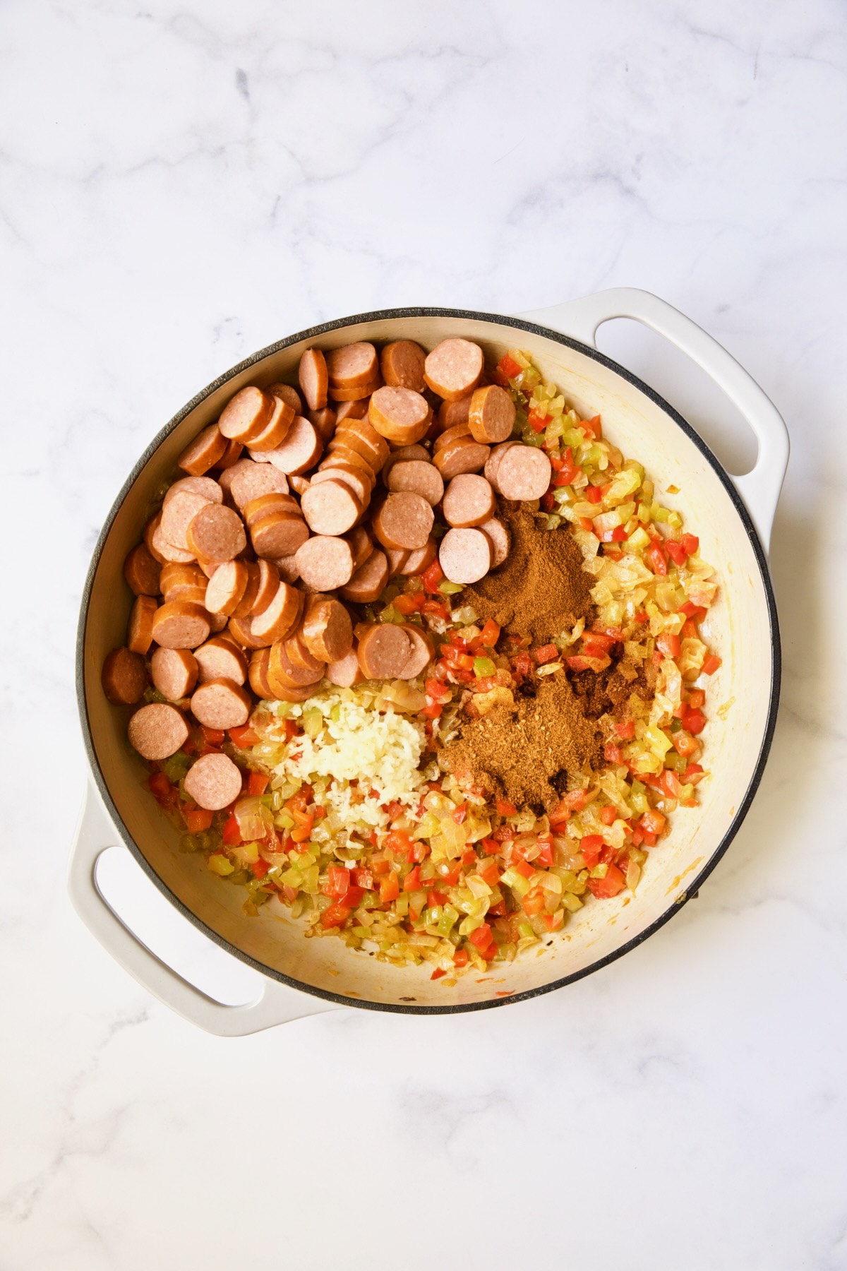 Andouille sausage , spices, onion, bell pepper and tomatoes in white enamel cast iron skillet.