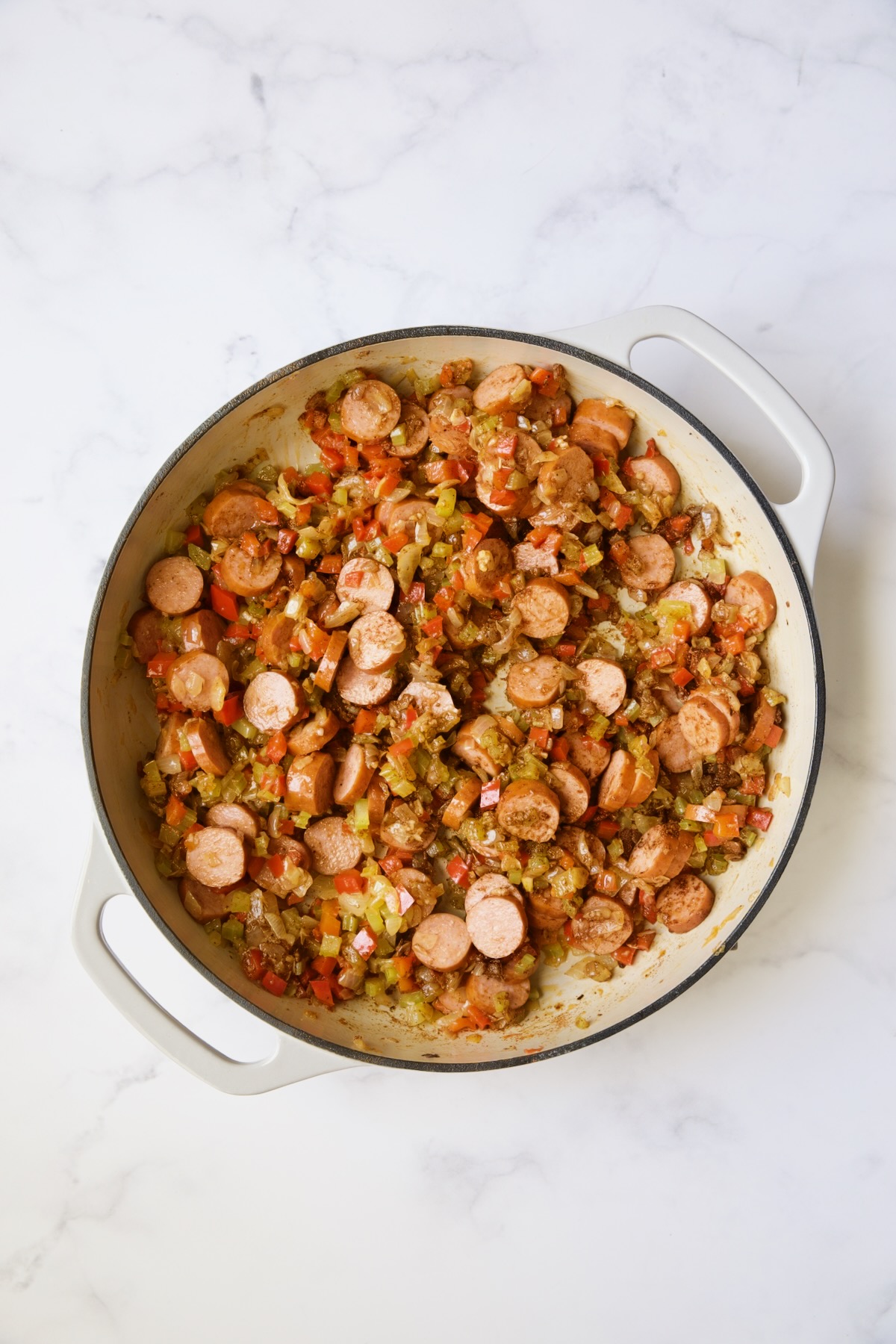 Sauteed vegetables and Andouille sausage in white cast iron enamel skillet.