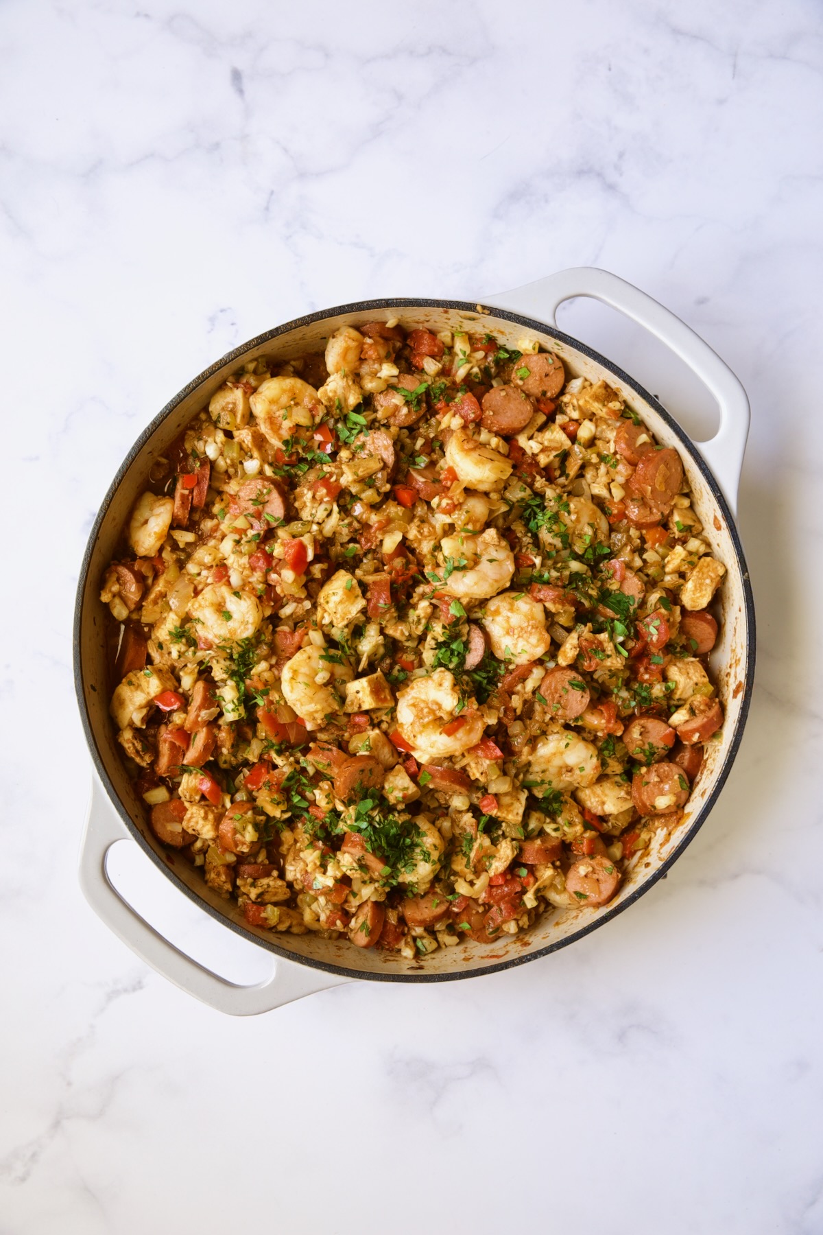 Finished Low-Carb Jambalaya with Chicken Shrimp and Sausage in white enamel cast iron skillet.