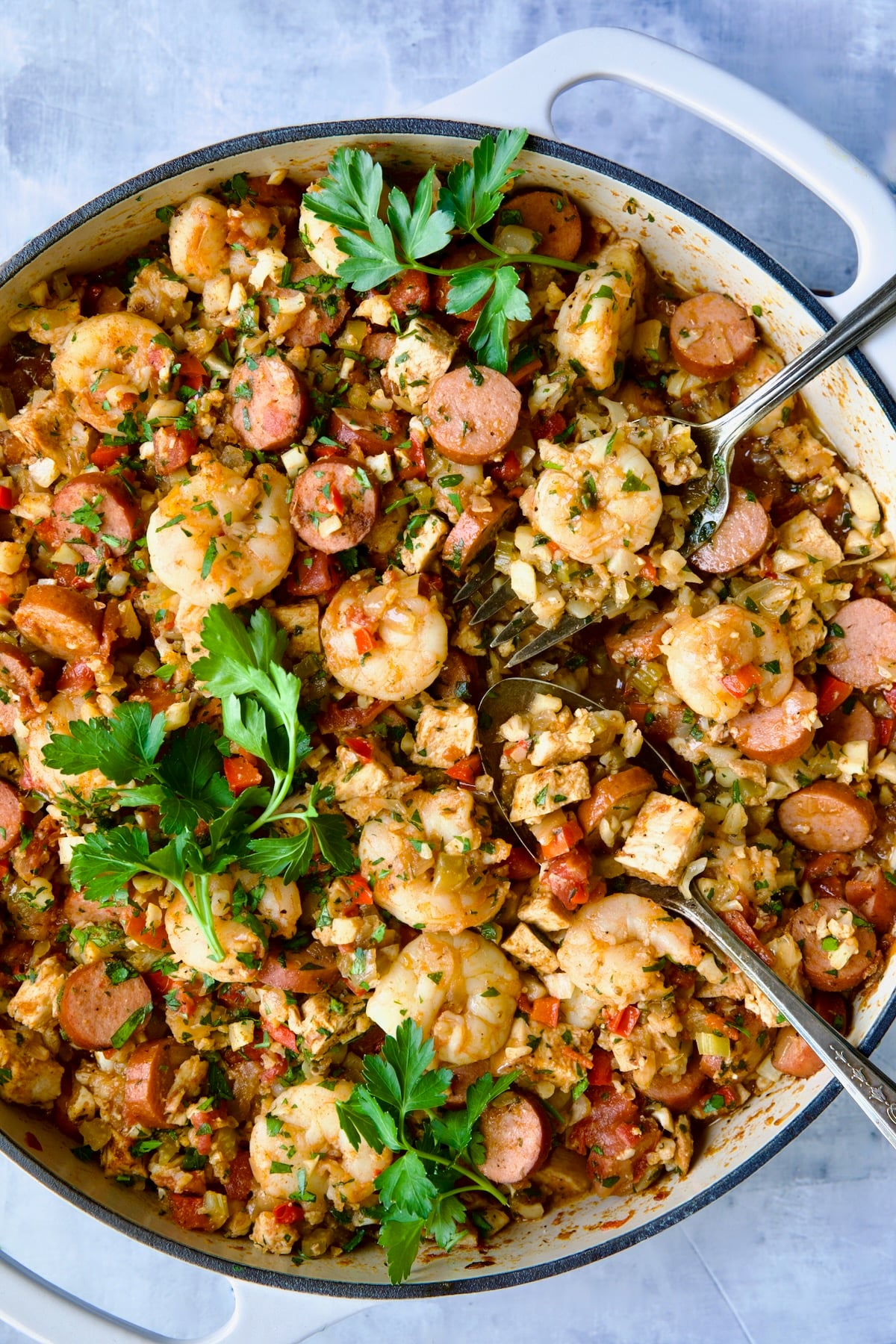 Low-Carb Jambalaya with Chicken Shrimp and Sausage with serving utensils garnished with fresh parsley.