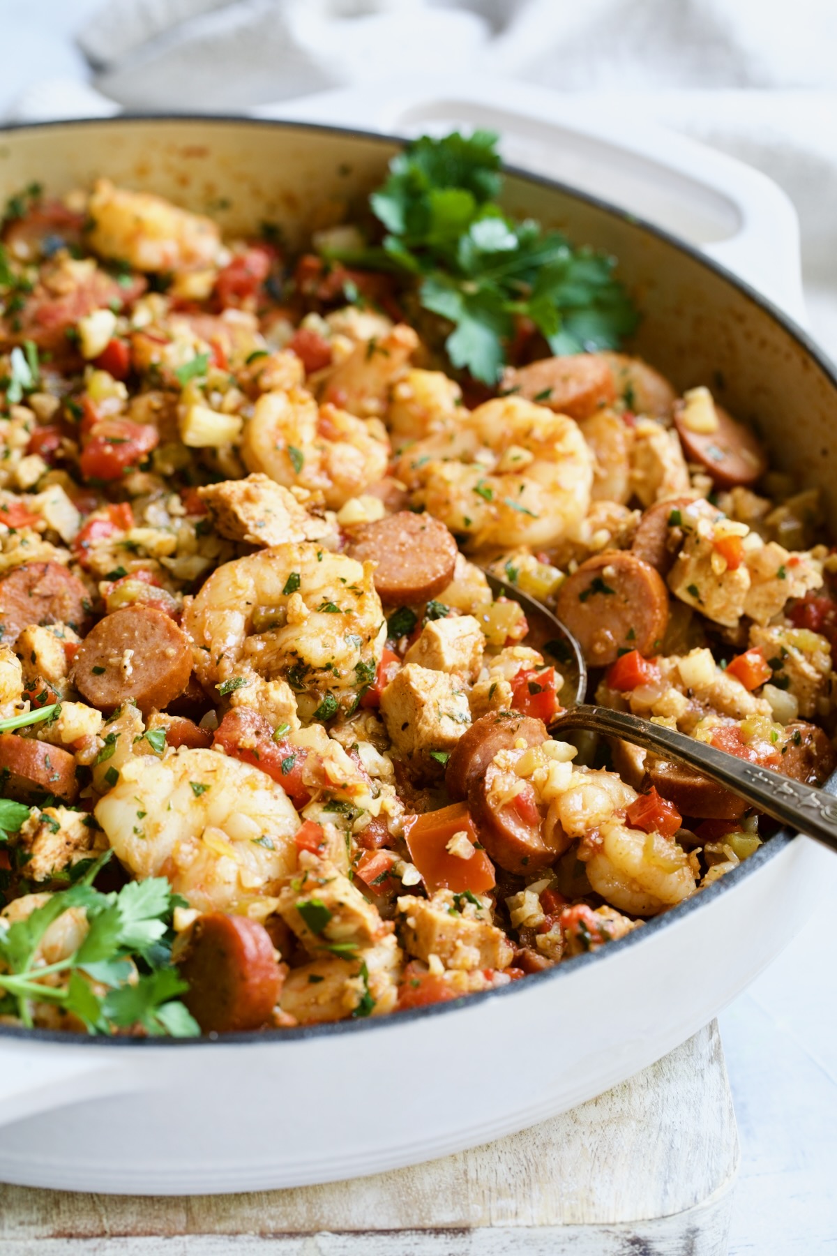 Low-Carb Jambalaya with Chicken Shrimp and Sausage in white enamel cast iron skillet with serving spoon.
