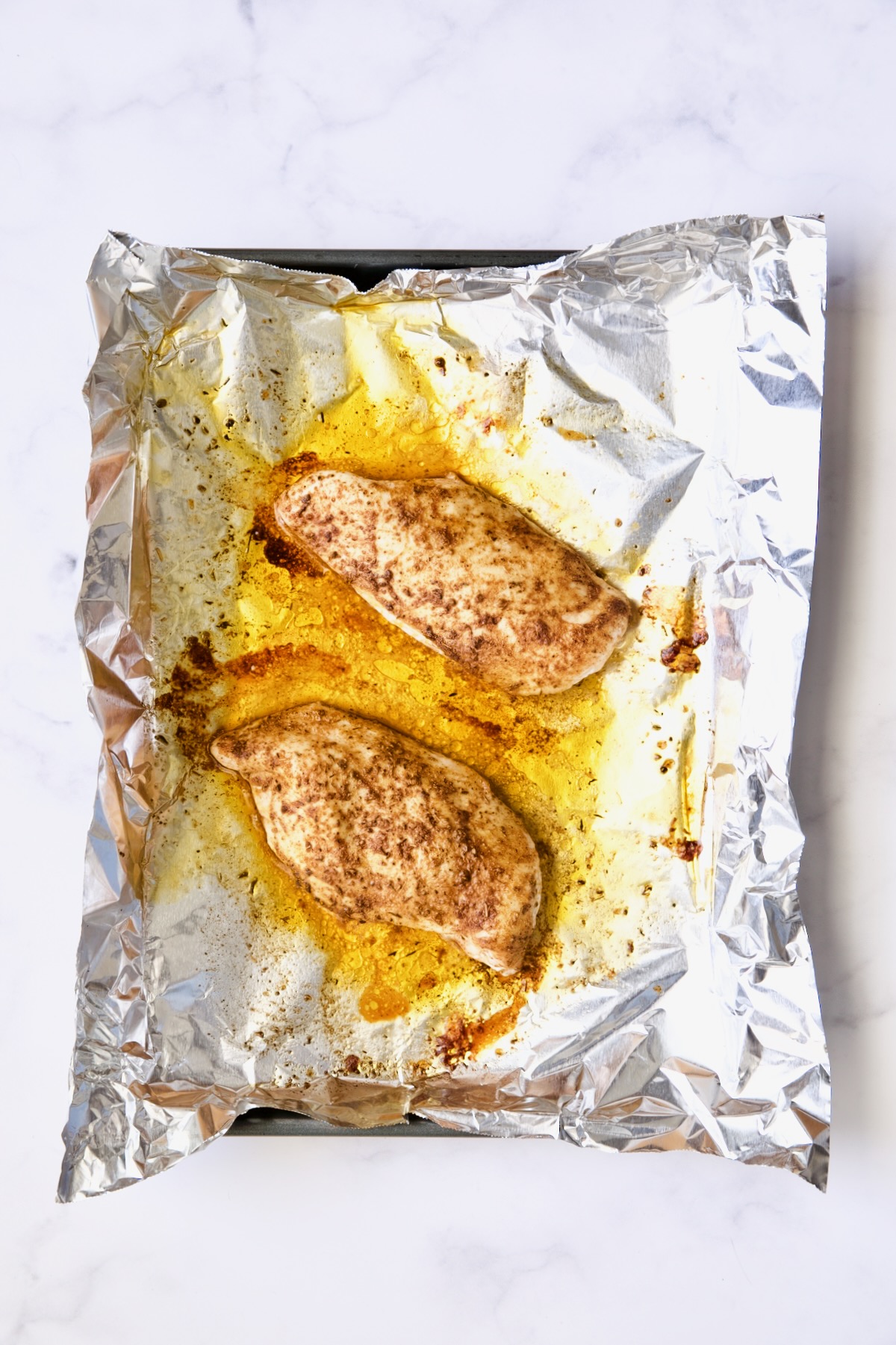 Cooked chicken breast halves on aluminum foil-lined rimmed baking sheet.