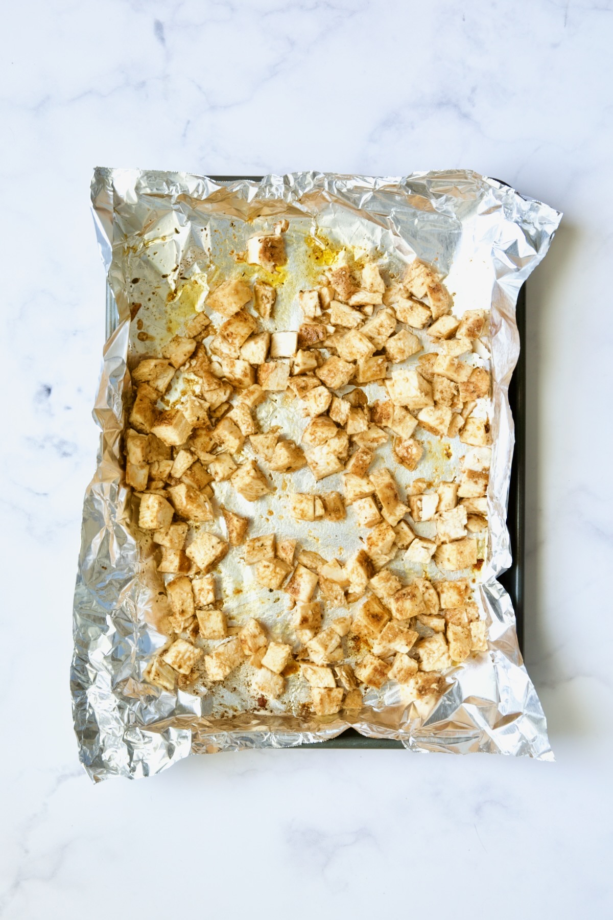 Cooked diced chicken on aluminum foil-lined rimmed baking sheet.