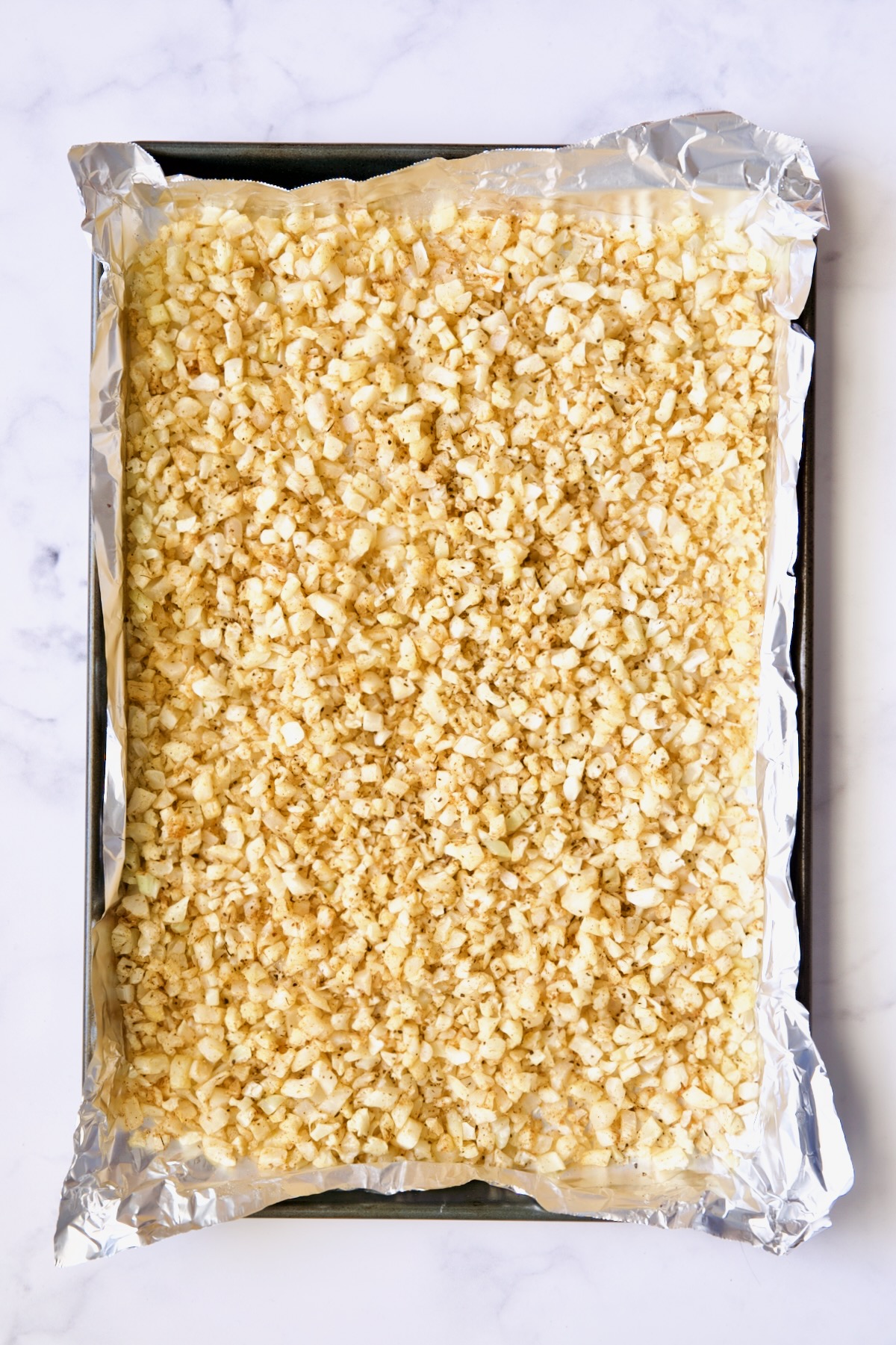 Cooked riced cauliflower on a sheet pan lined with aluminum foil.