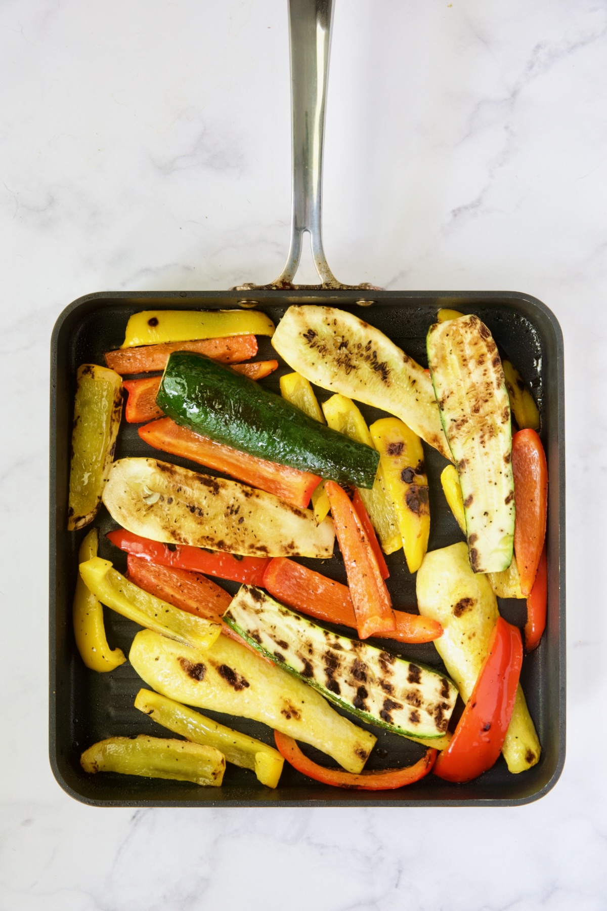 Grilled zucchini, yellow squash and bell peppers on square grill pan.