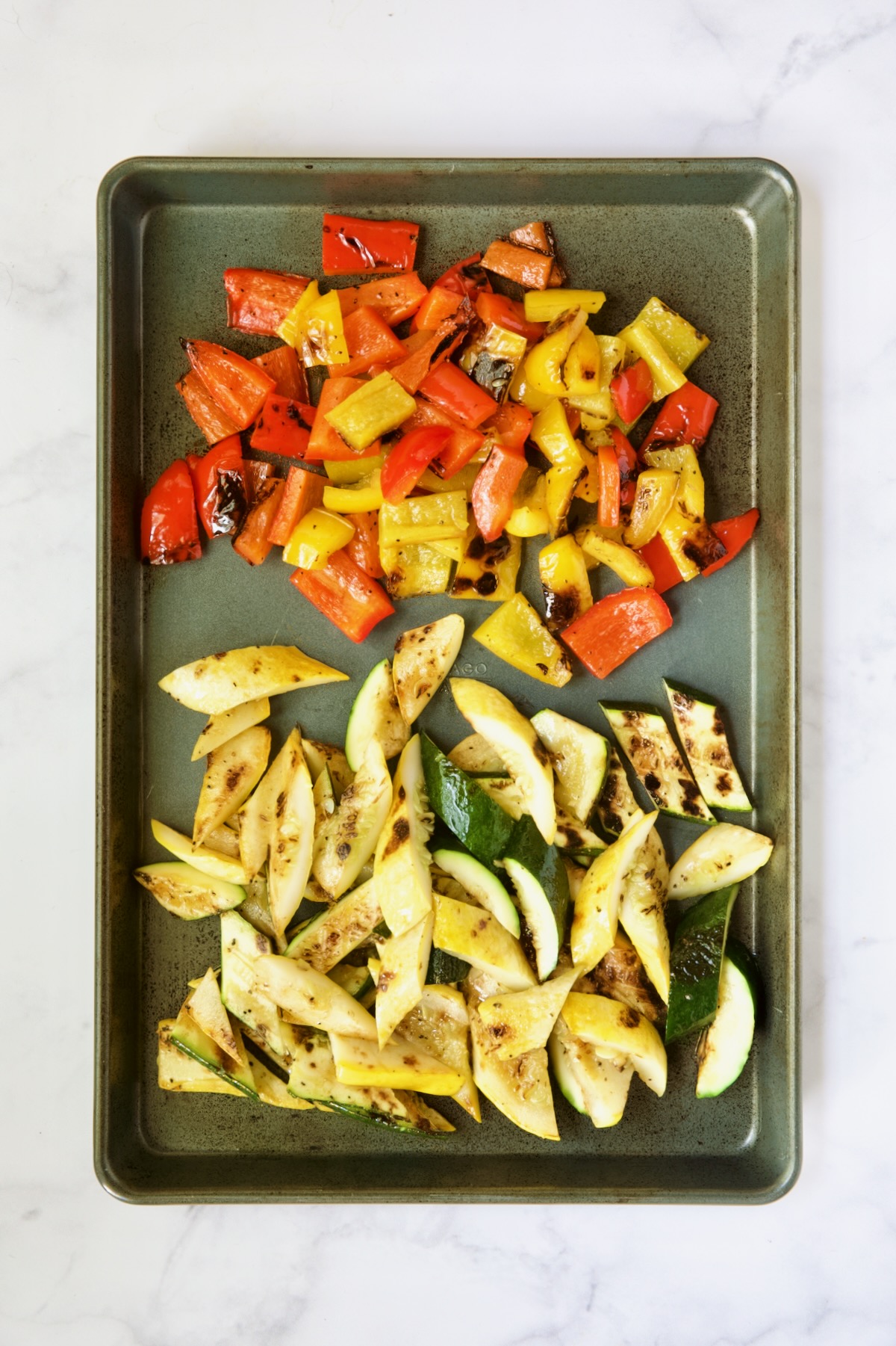 Grilled, cut zucchini, yellow squash and bell peppers on rimmed sheet pan.