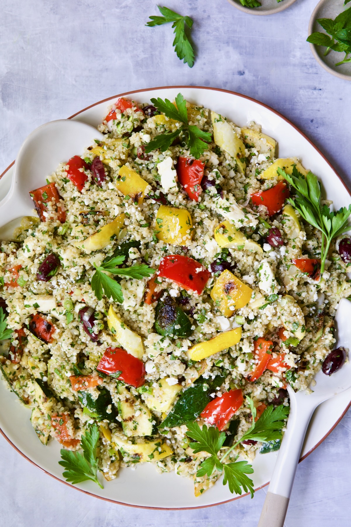 Mediterranean Quinoa Salad with Grilled Vegetables on round white platter garnished with parsley sprigs.